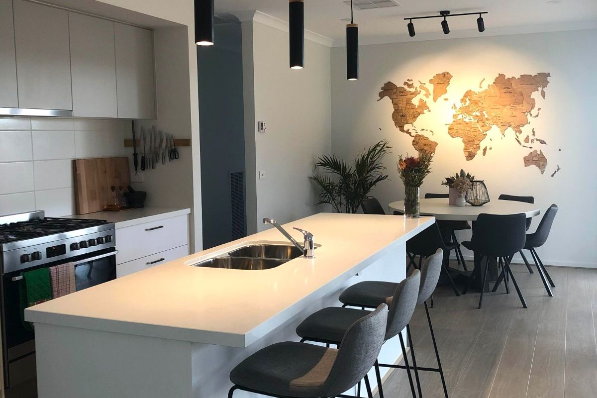 Modern kitchen with white island, sink, bar stools, wooden world map wall decor, and dining area