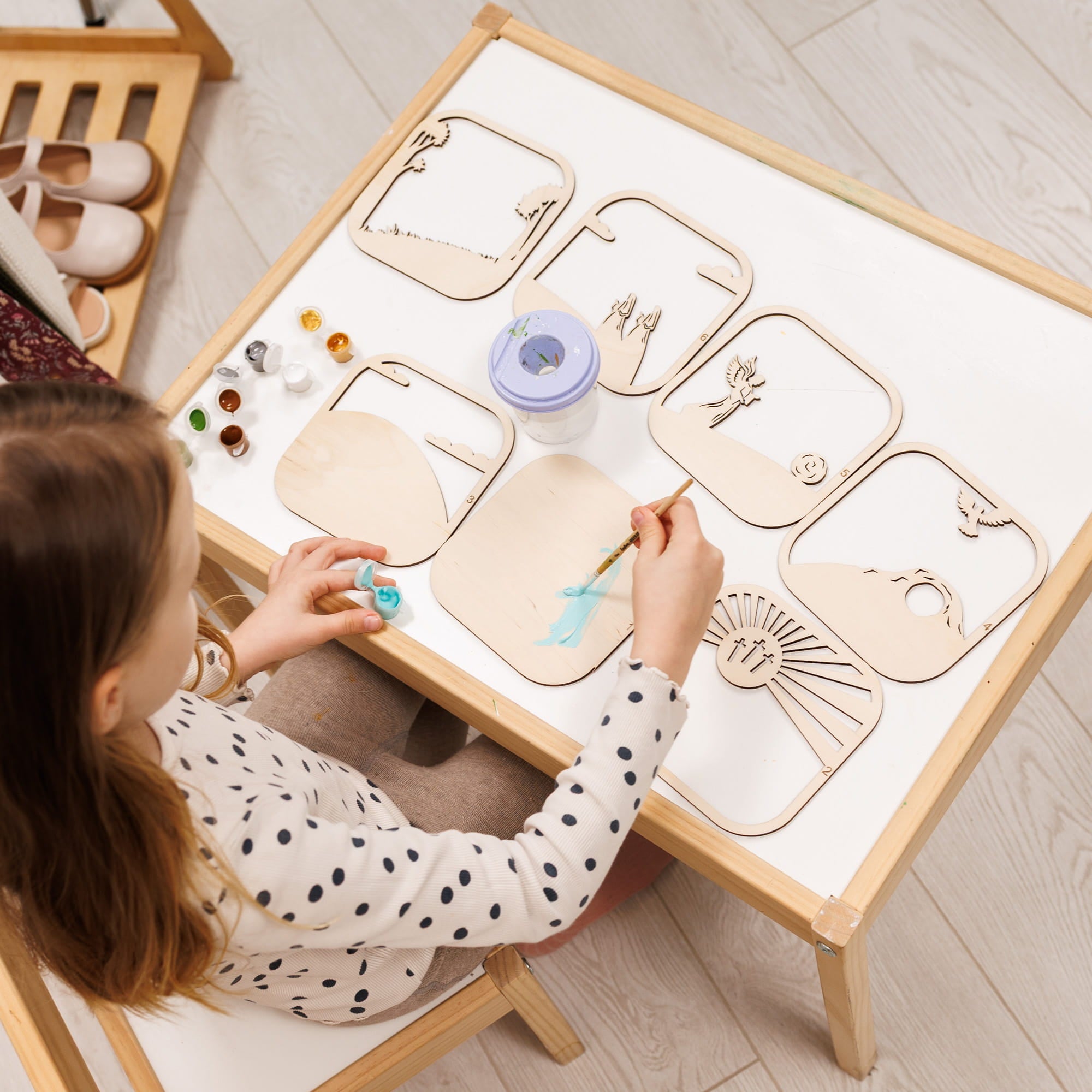 Child painting on a wooden art easel with various art supplies.