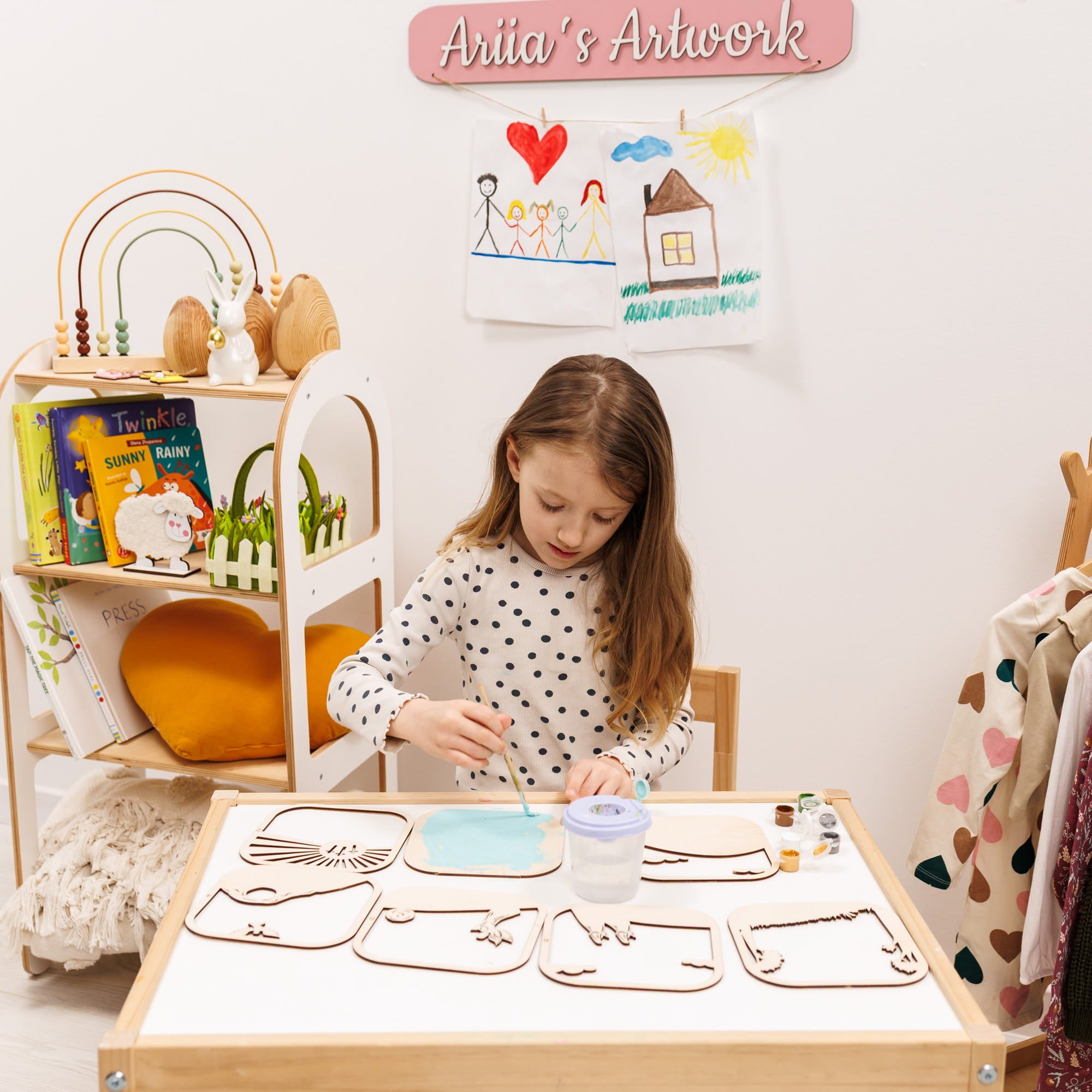 Child at a table with art supplies and drawings on the wall, labeled 'Anita's Artwork'.