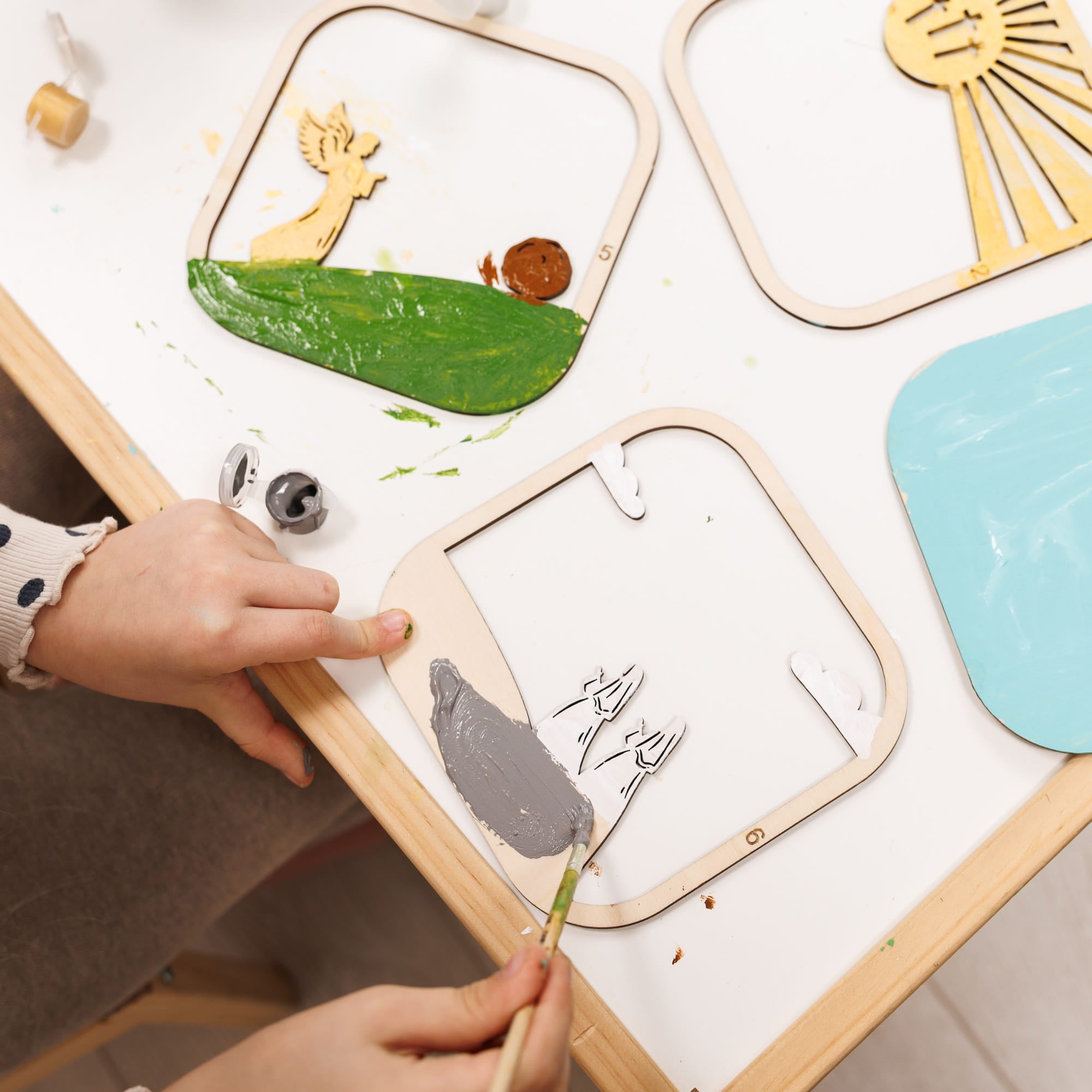 Child's hand interacting with a wooden craft set on a white surface