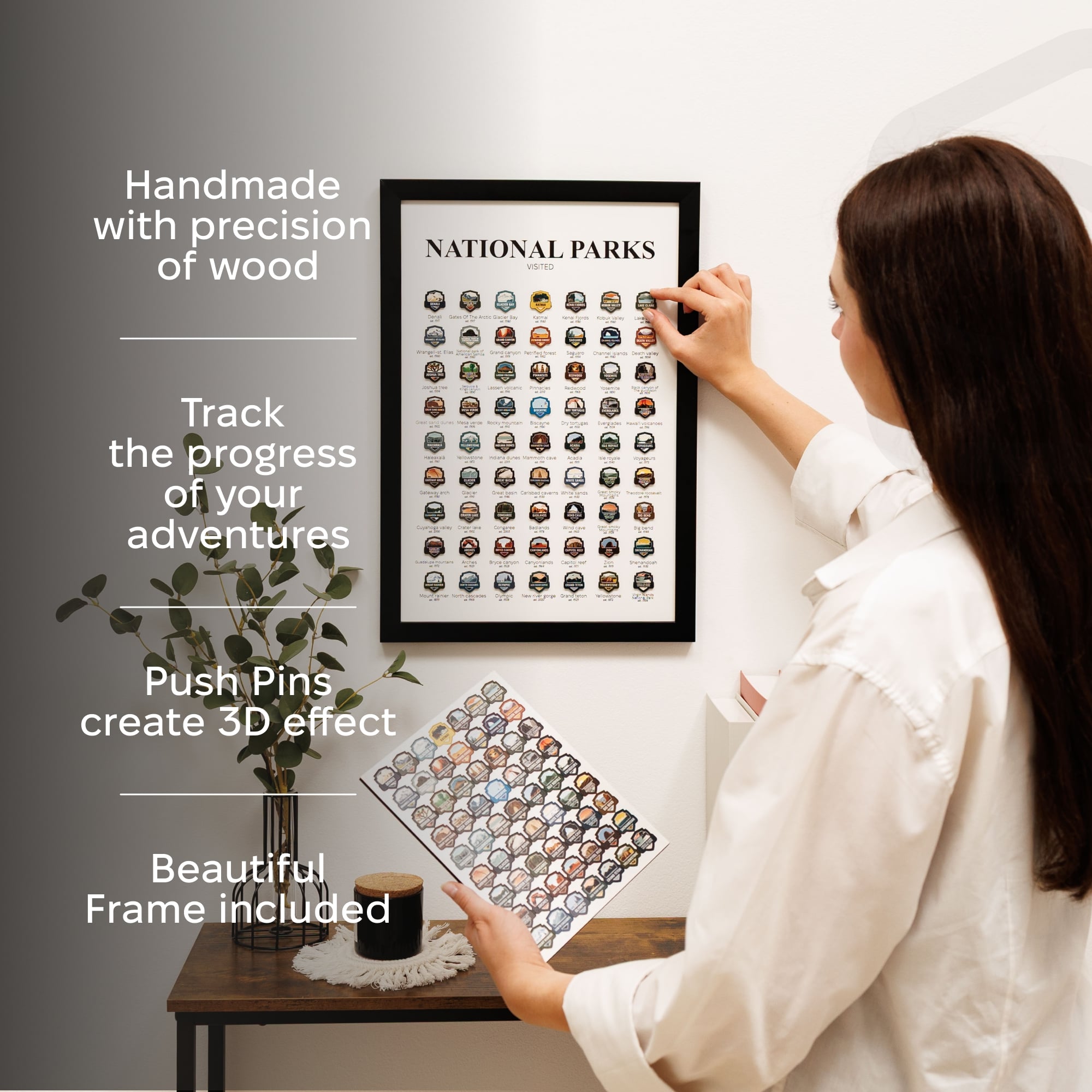 Woman hanging a framed National Parks travel map with push pins on a wall.