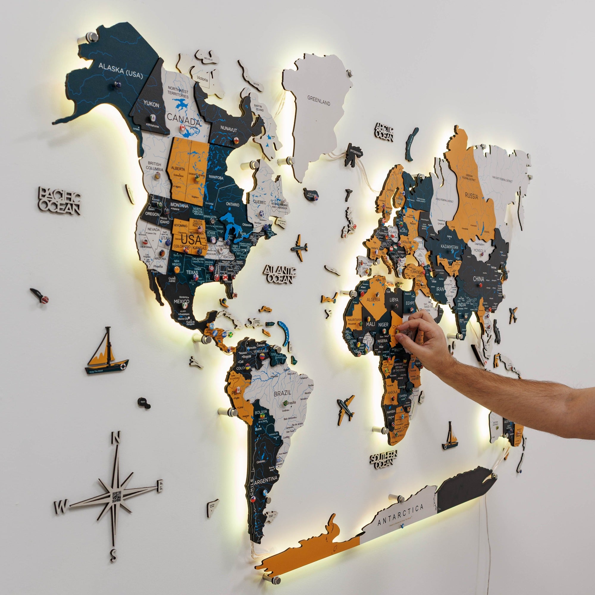 World map wall decoration with illuminated edges and a hand interacting with it.