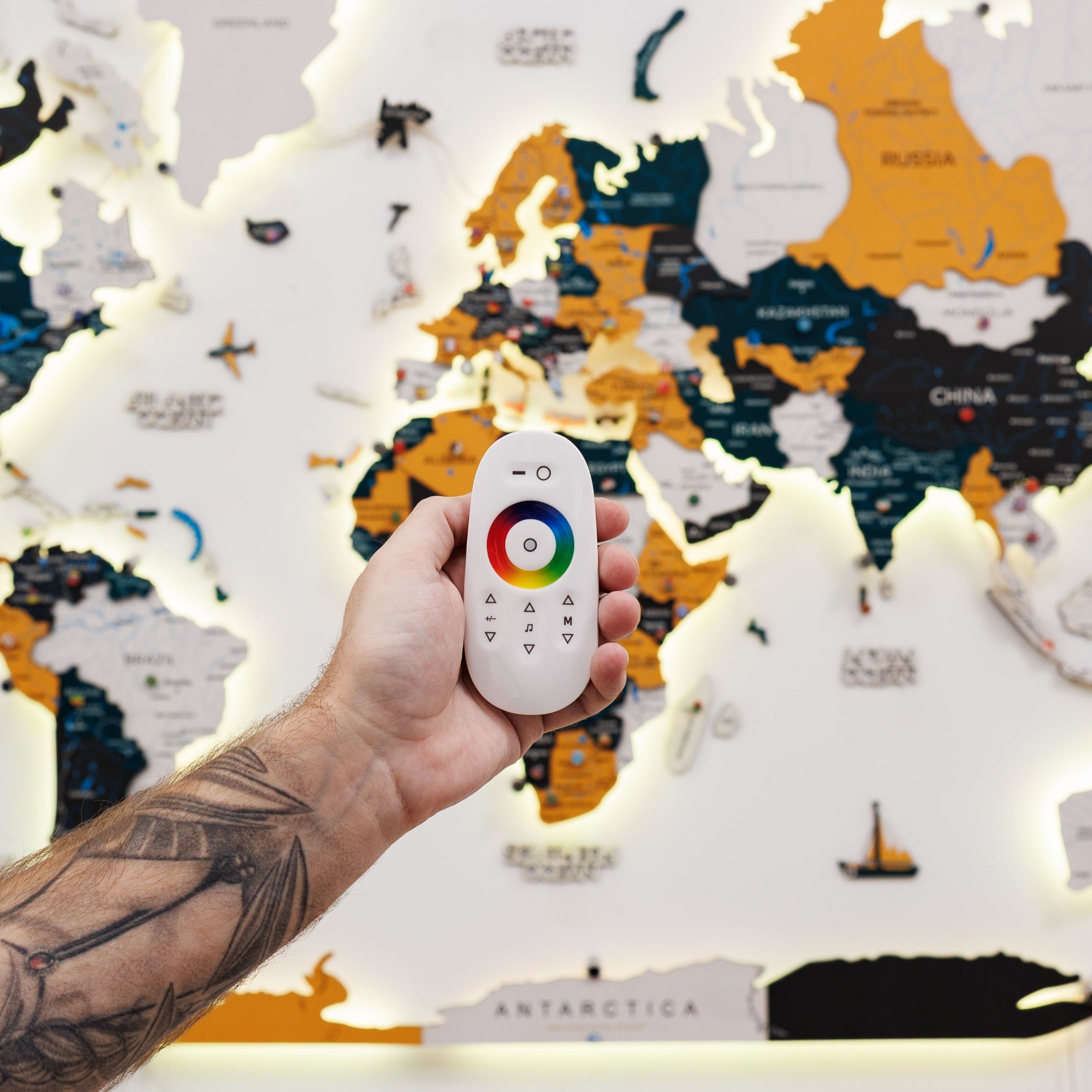 Hand holding a remote control with color options in front of a world map