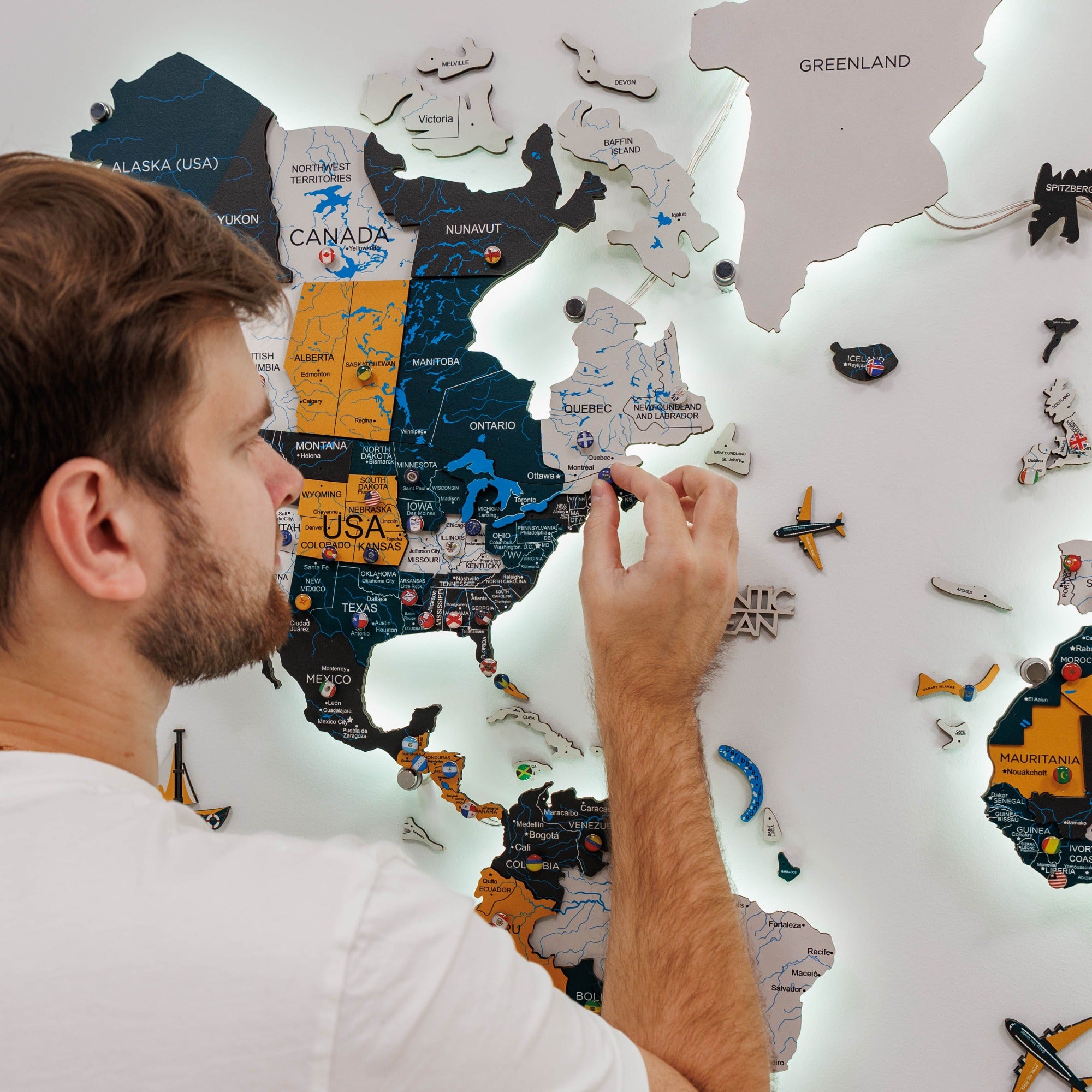Man assembling a wooden puzzle map of the world on a wall.