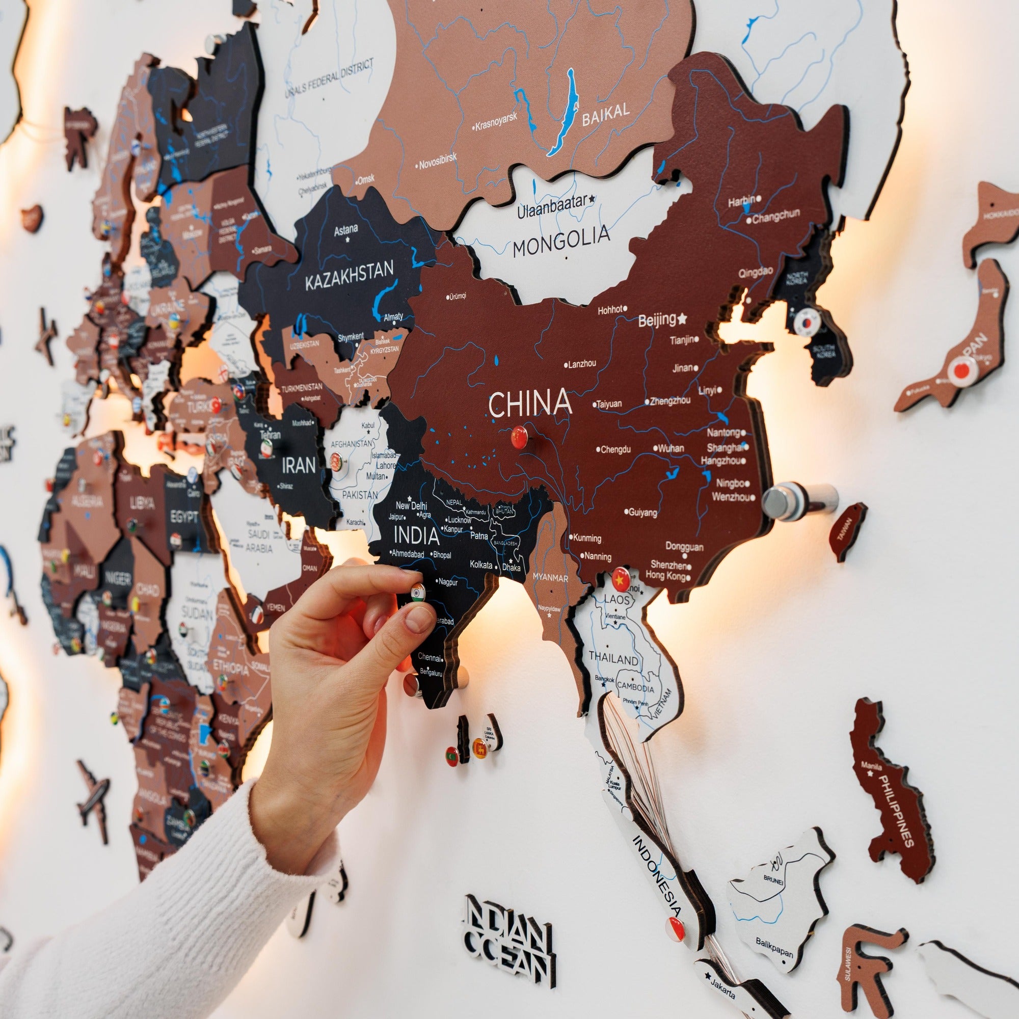 Wooden world map puzzle with a hand placing a piece labeled 'India'.