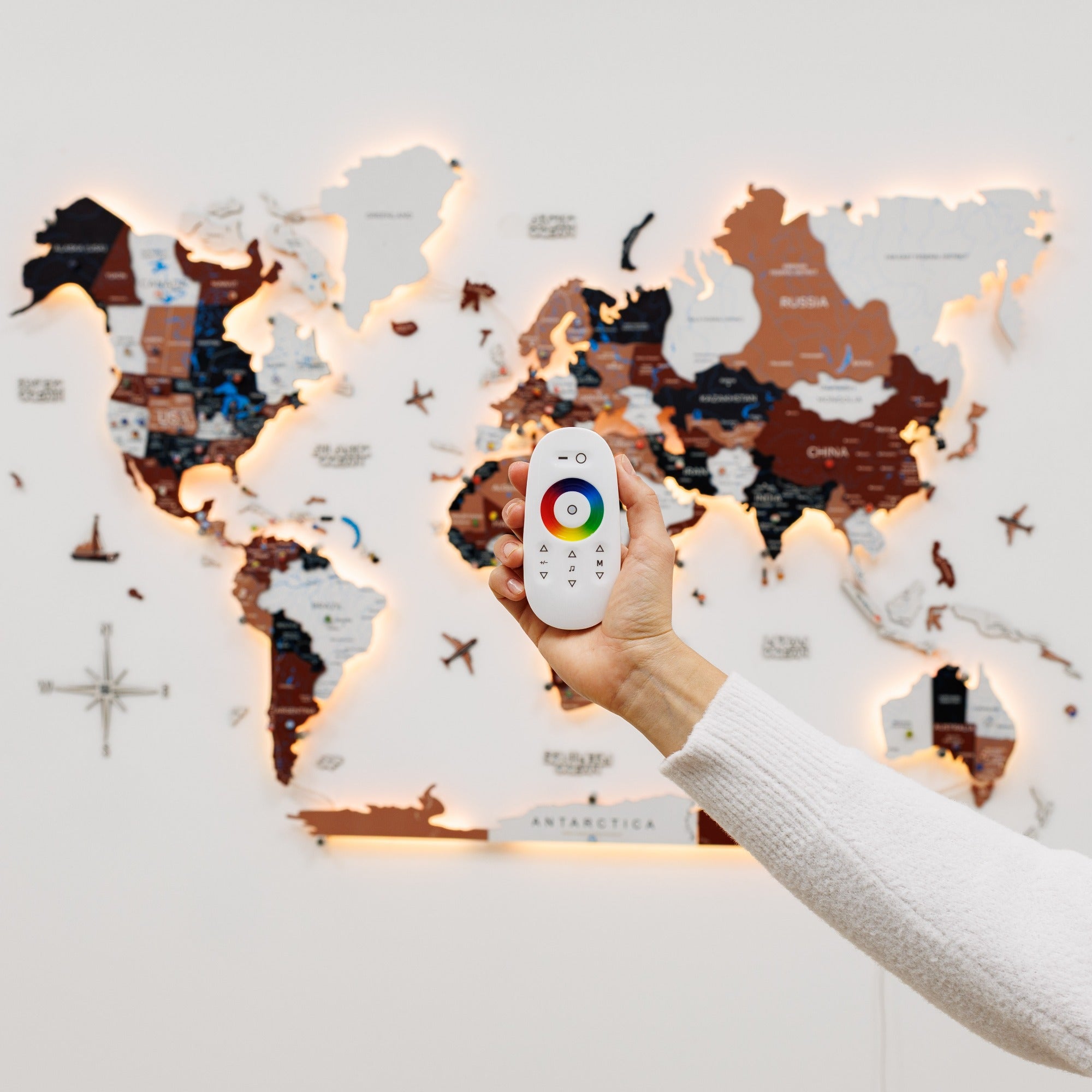 Hand holding a remote control with color display in front of a world map