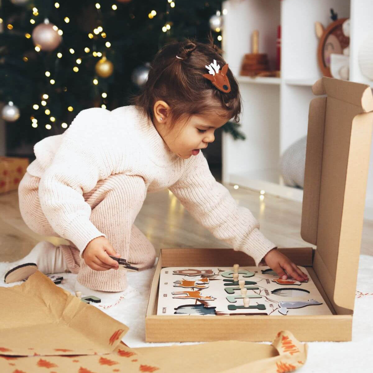 Child playing with a puzzle in front of a decorated Christmas tree.