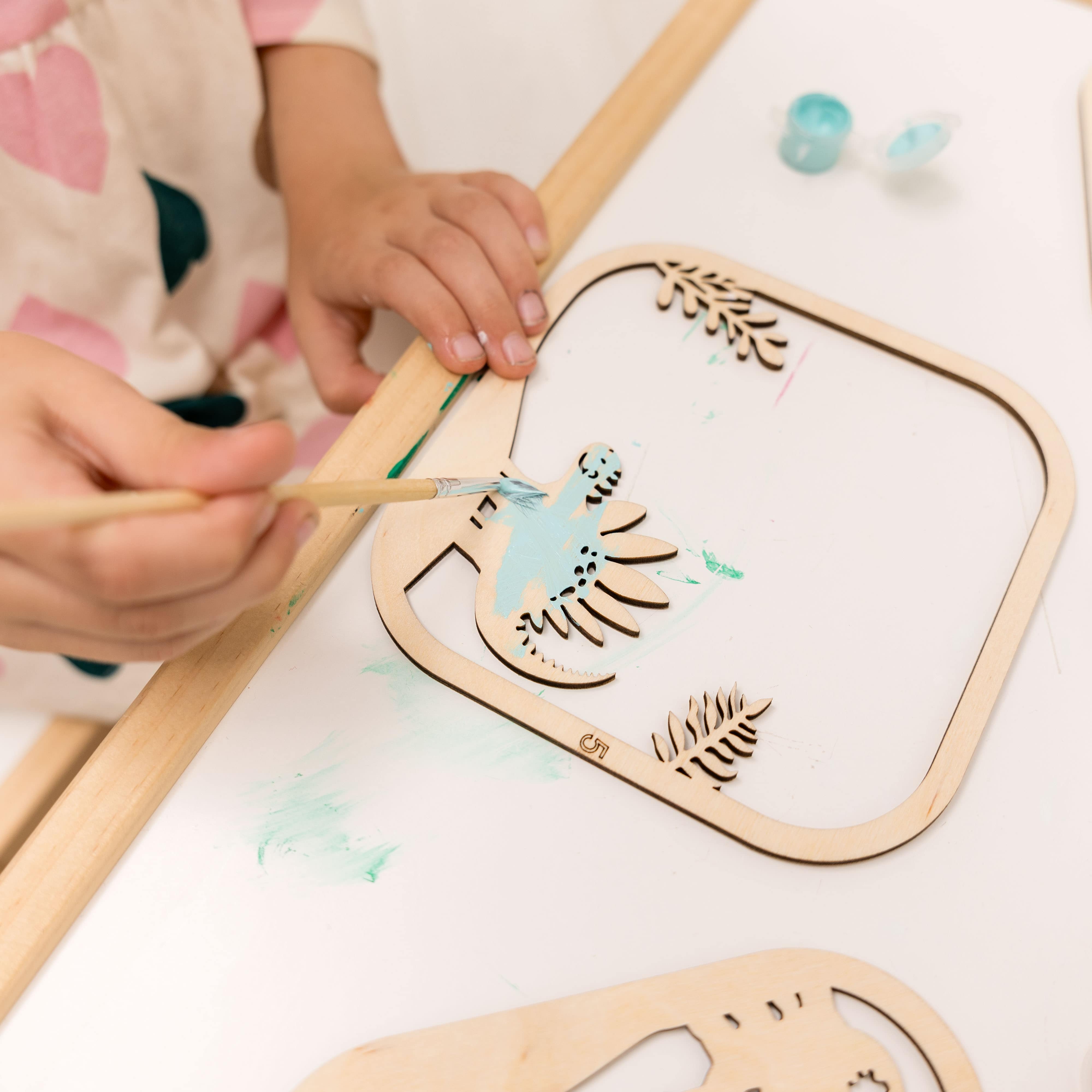 Child's hands using a paintbrush to color a wooden craft with a fairy design.