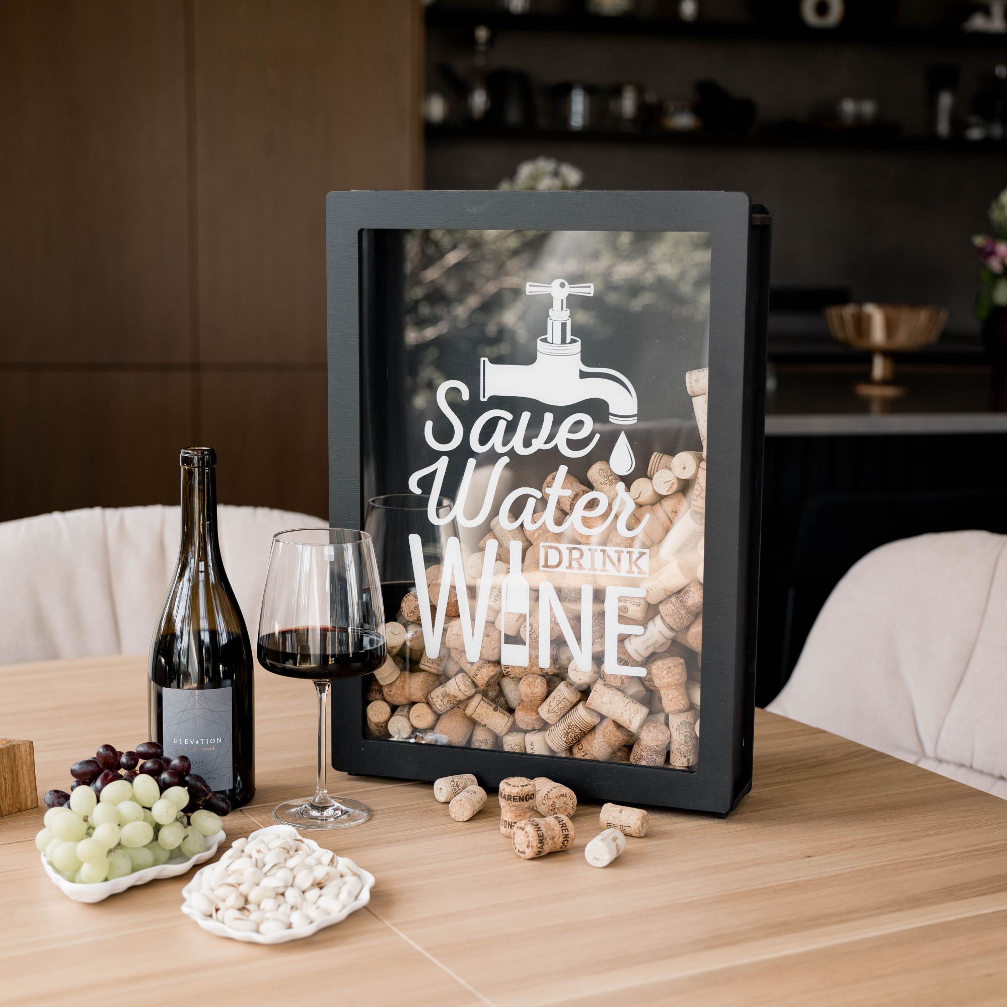Wooden wine cork holder shadow box standing on dining table, filled with corks, wine bottle and snacks nearby – rustic and modern wine decoration gift.
