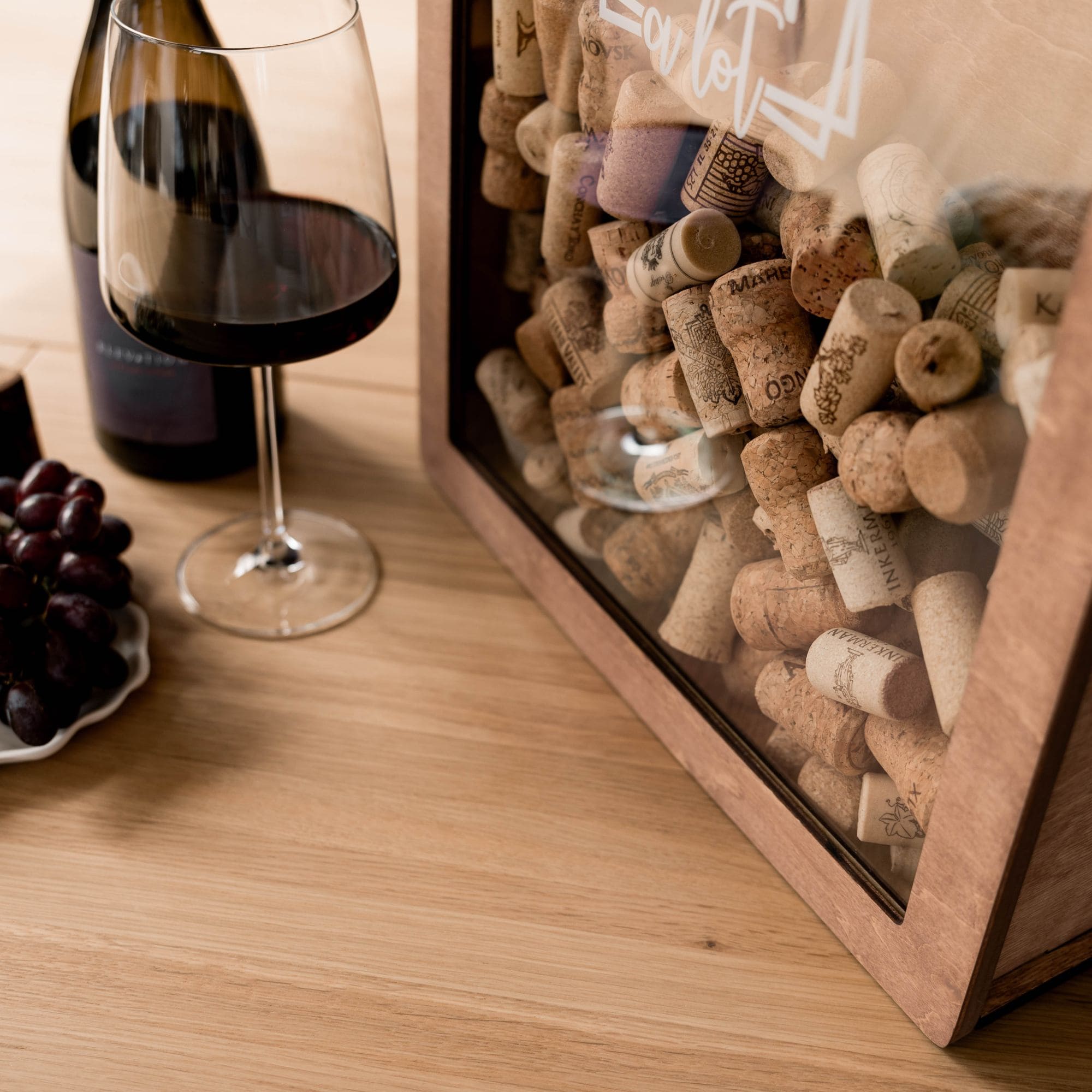 Close-up of wooden wine cork holder box with corks, glass of red wine and grapes on the table