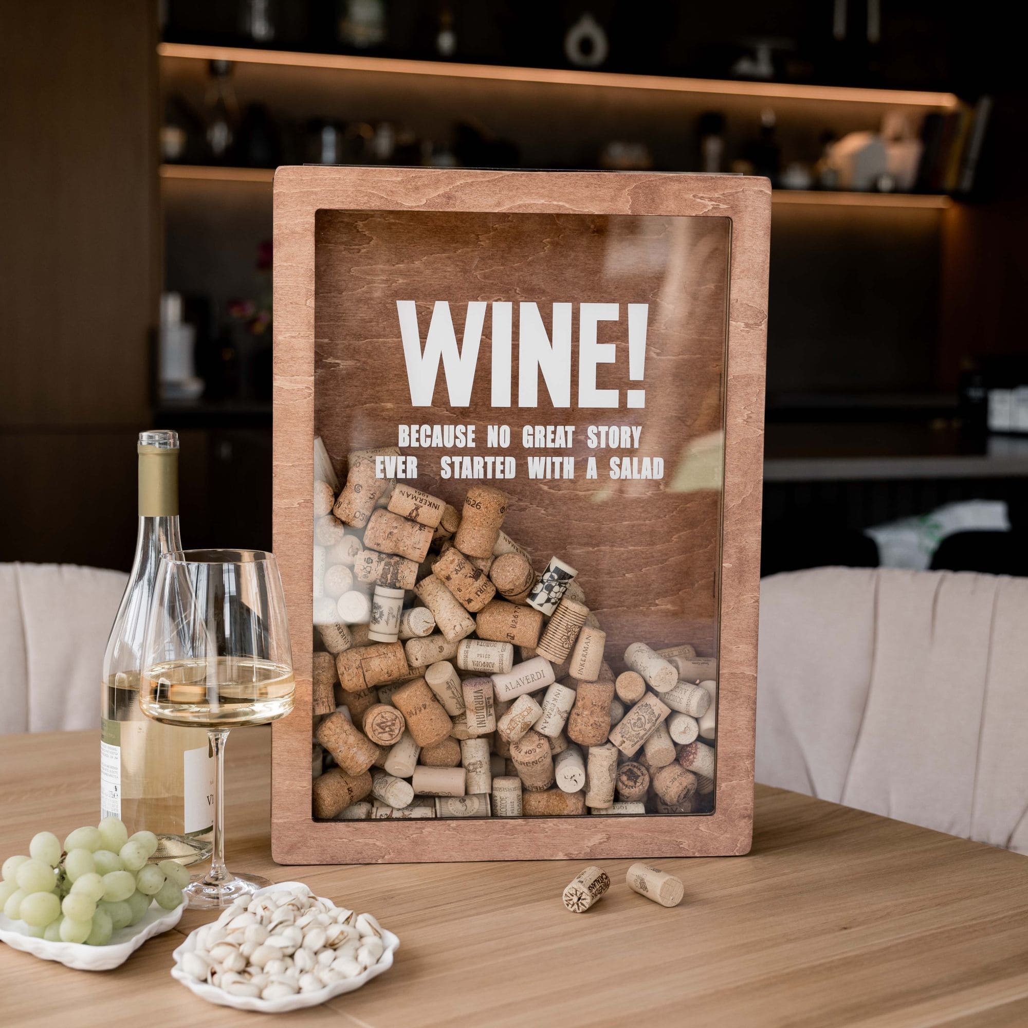 A wooden wine cork box with the text 'WINE! Because no great story ever started with a salad' displayed on a table with wine and snacks.