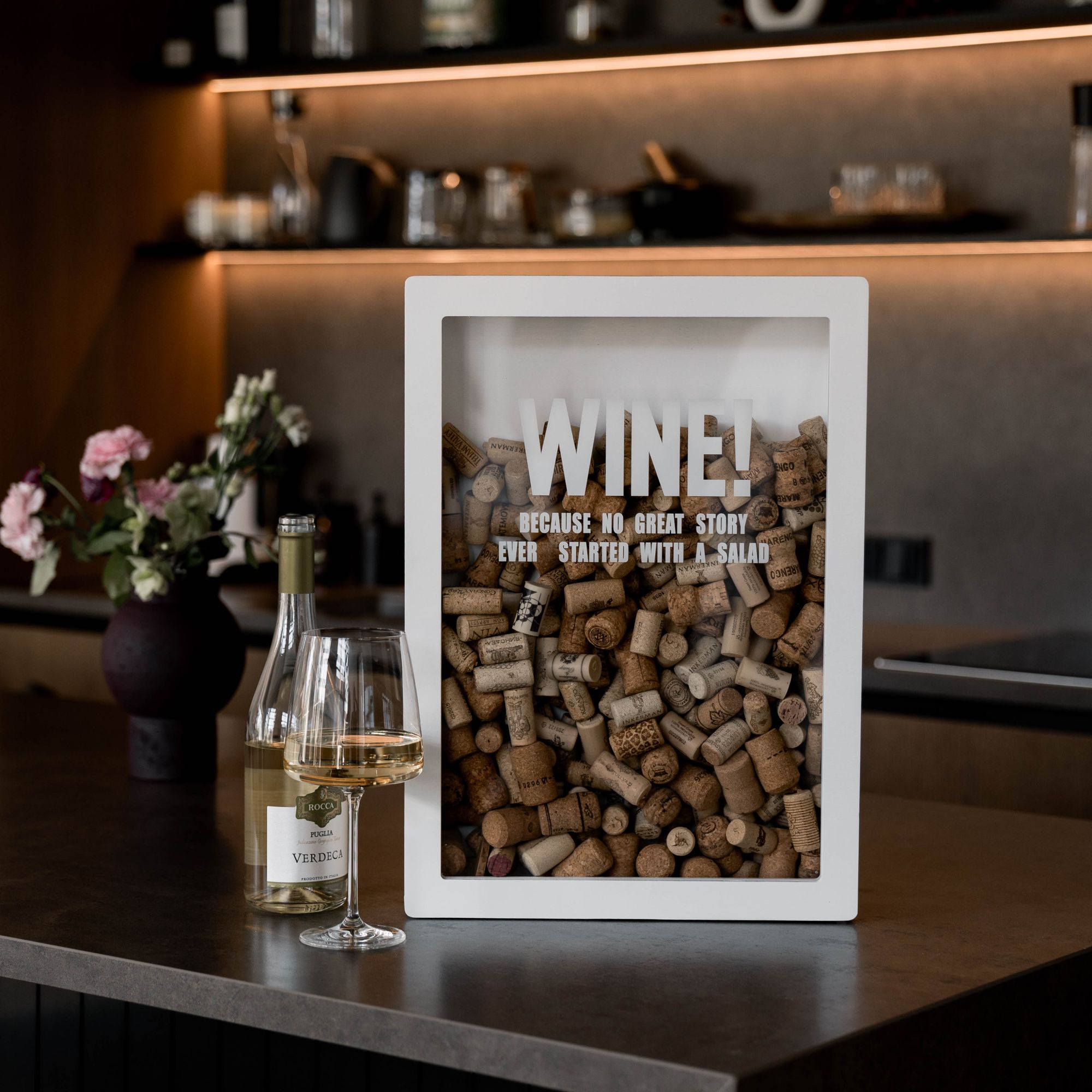 White wooden wine cork shadow box with glass of white wine and wine bottle in modern kitchen