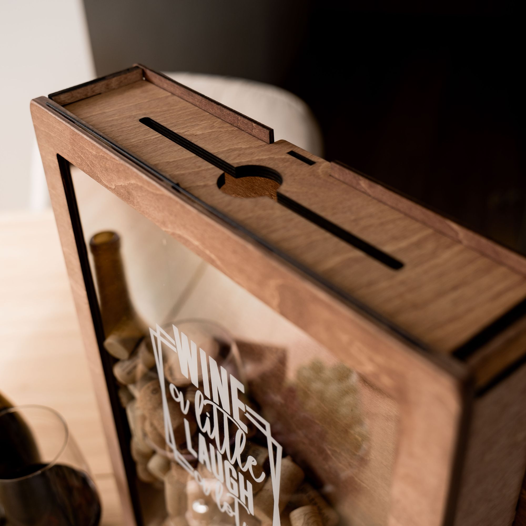 Close-up of the top of a wooden cork holder with a slot for dropping wine corks, designed with the phrase "Wine a little, laugh a lot".