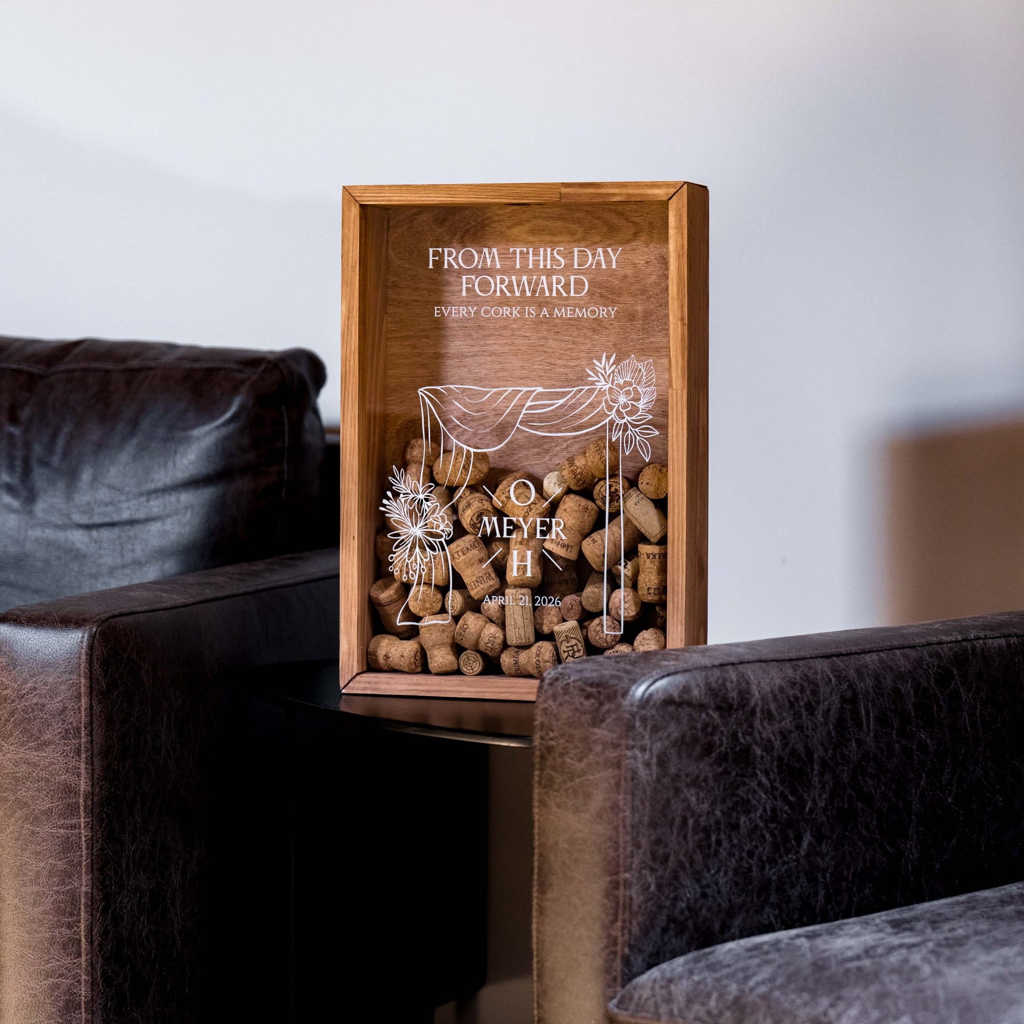 A wooden shadow box display filled with wine corks, placed on a dark leather sofa in a living room setting.