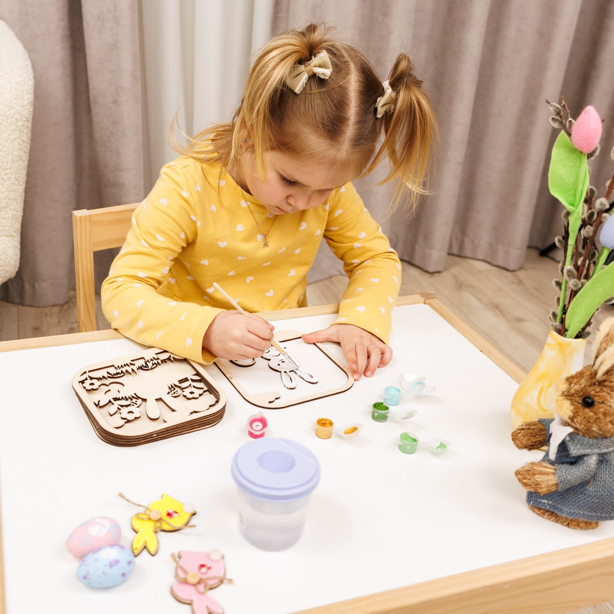 Child in a yellow polka dot shirt playing with wooden letters on a table.