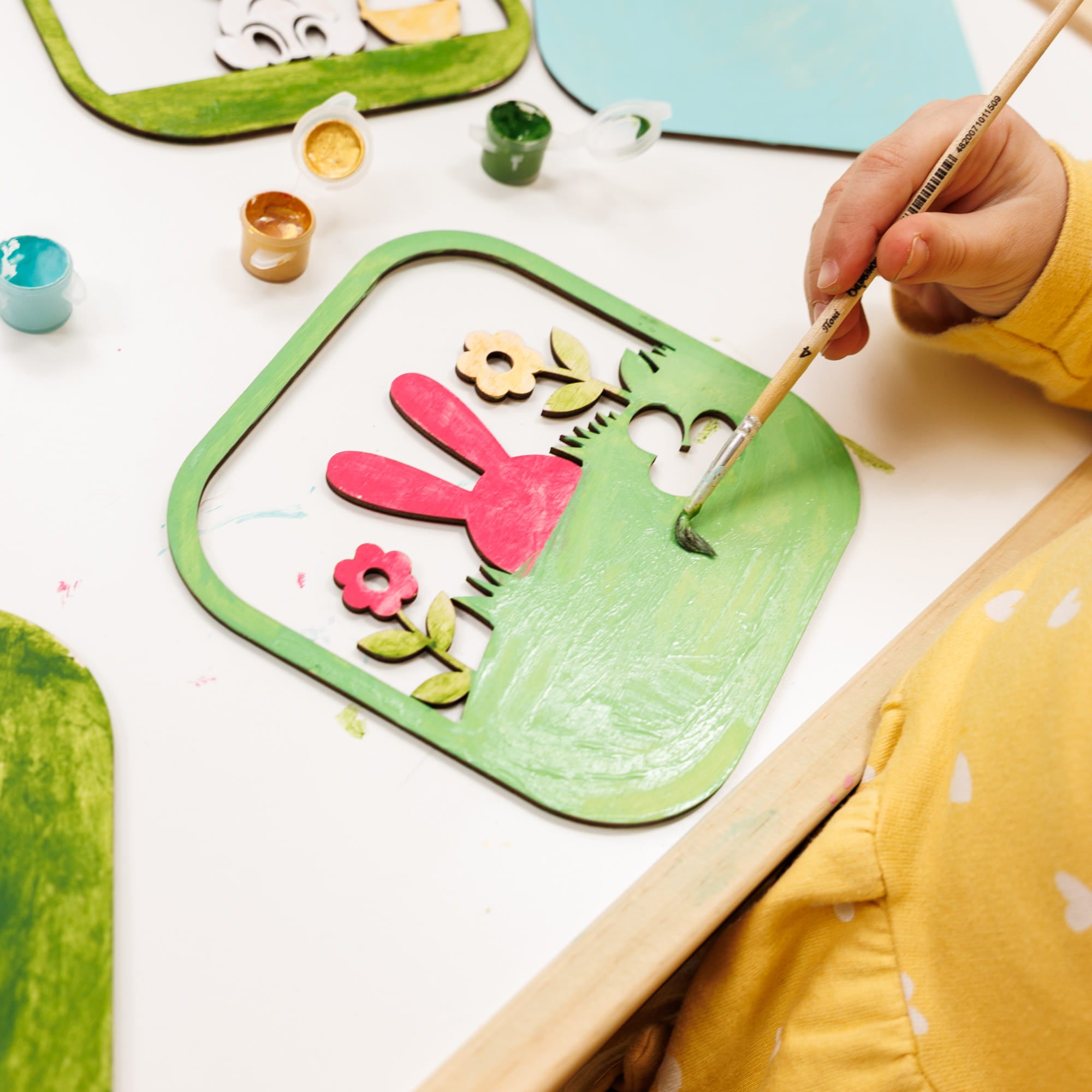 Child painting a craft project with colorful materials on a white table.