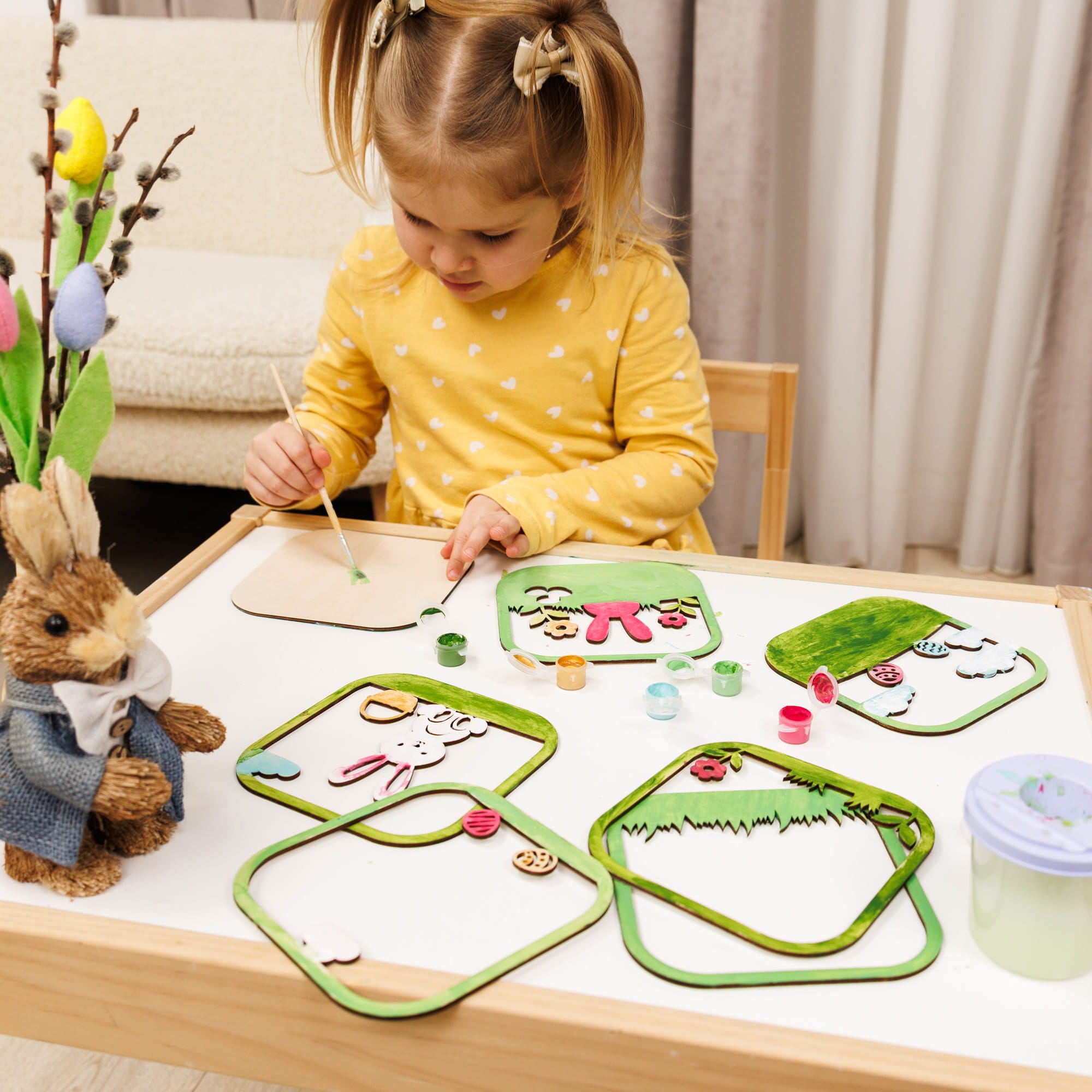 Child painting on a table with craft materials and a toy rabbit.