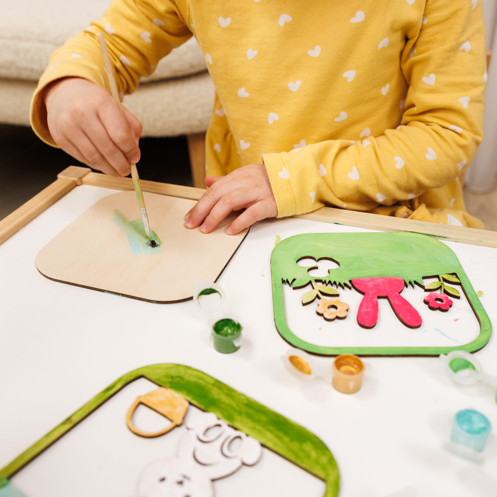 Child painting on a wooden board with colorful templates on a table.