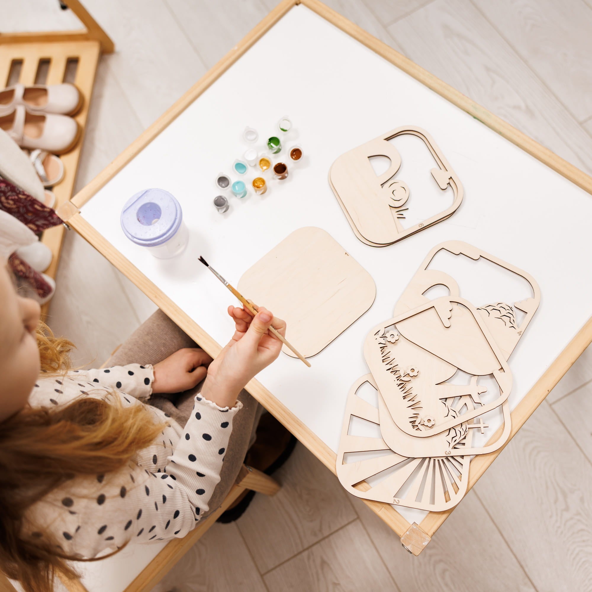 Child painting on a wooden board with various shapes and colors