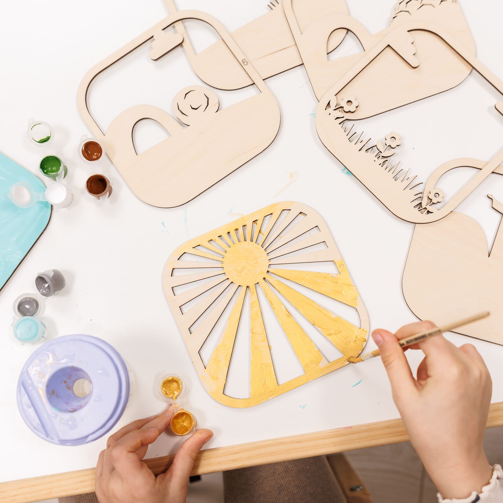 Person painting wooden cutouts on a table with paint supplies.
