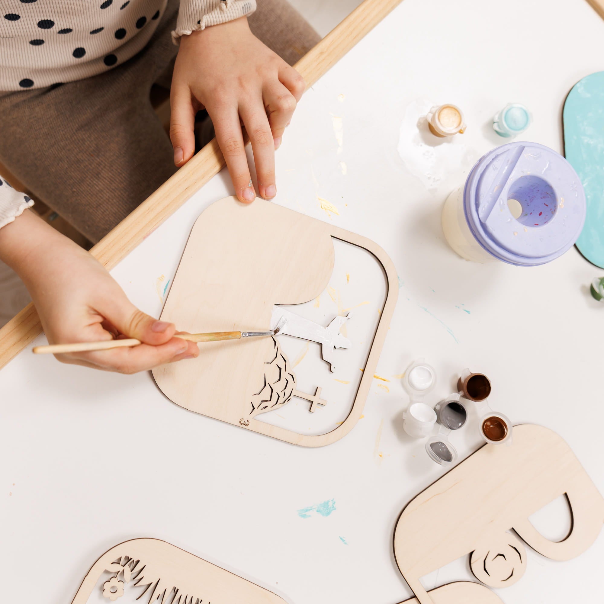 Person painting wooden animal shapes with paint supplies on a table.