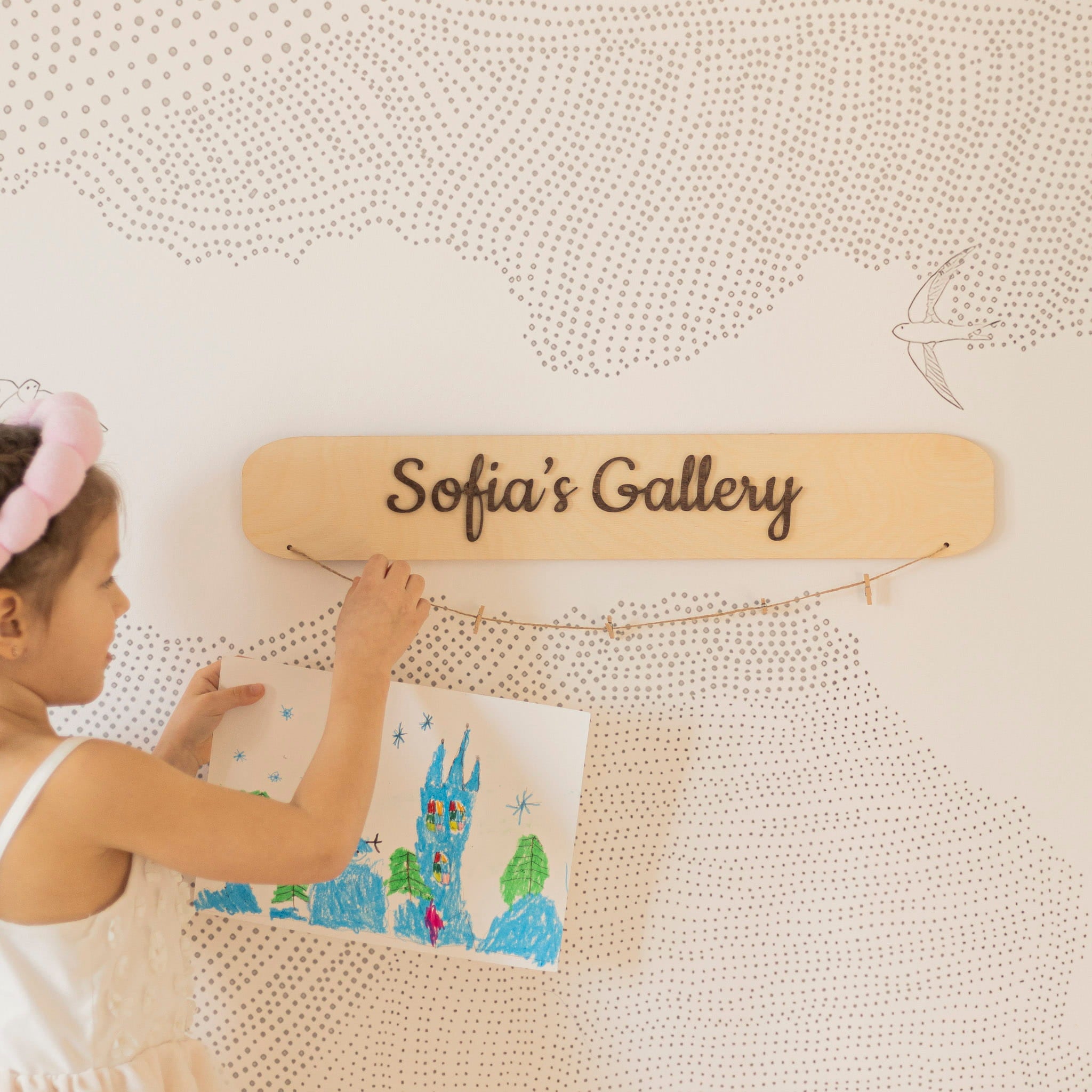 Child hanging a drawing on a wall with 'Sofia's Gallery' sign