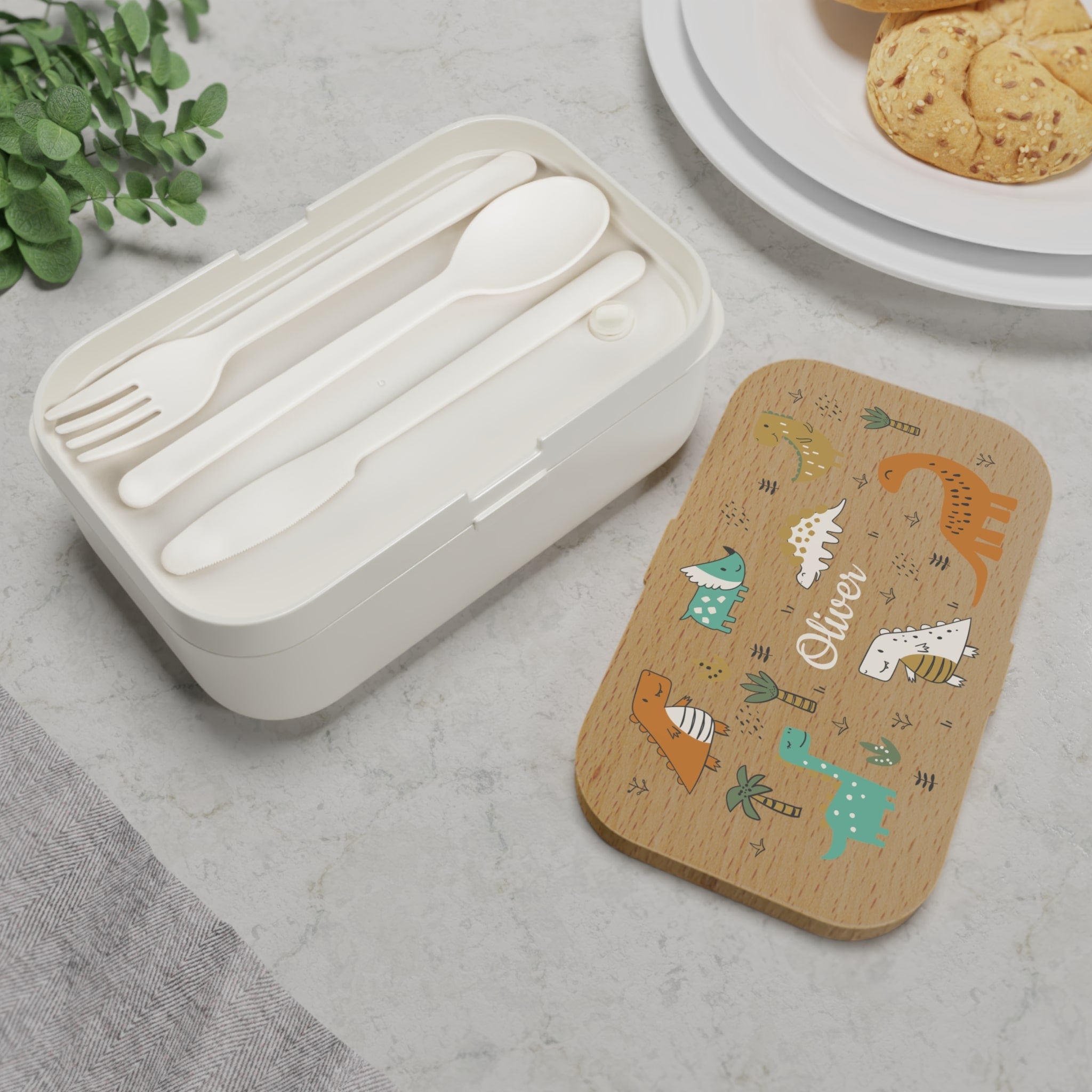 Set of white cutlery in a white container with a wooden lid featuring animal illustrations on a gray surface.