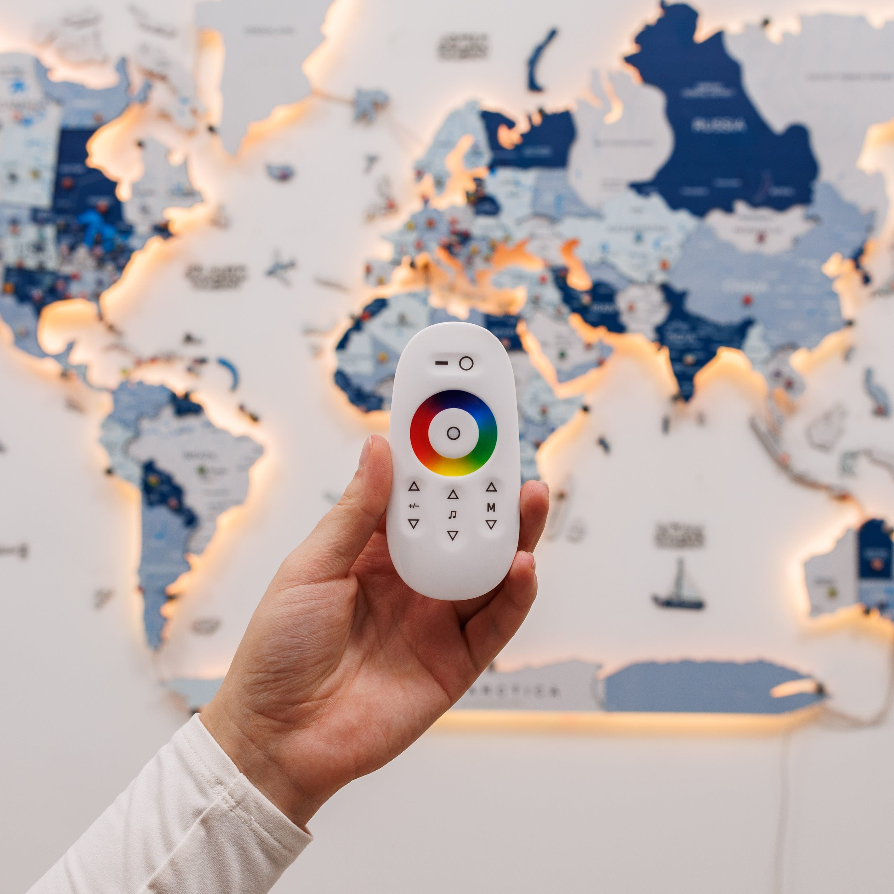 Hand holding a white remote control with color wheel in front of a world map