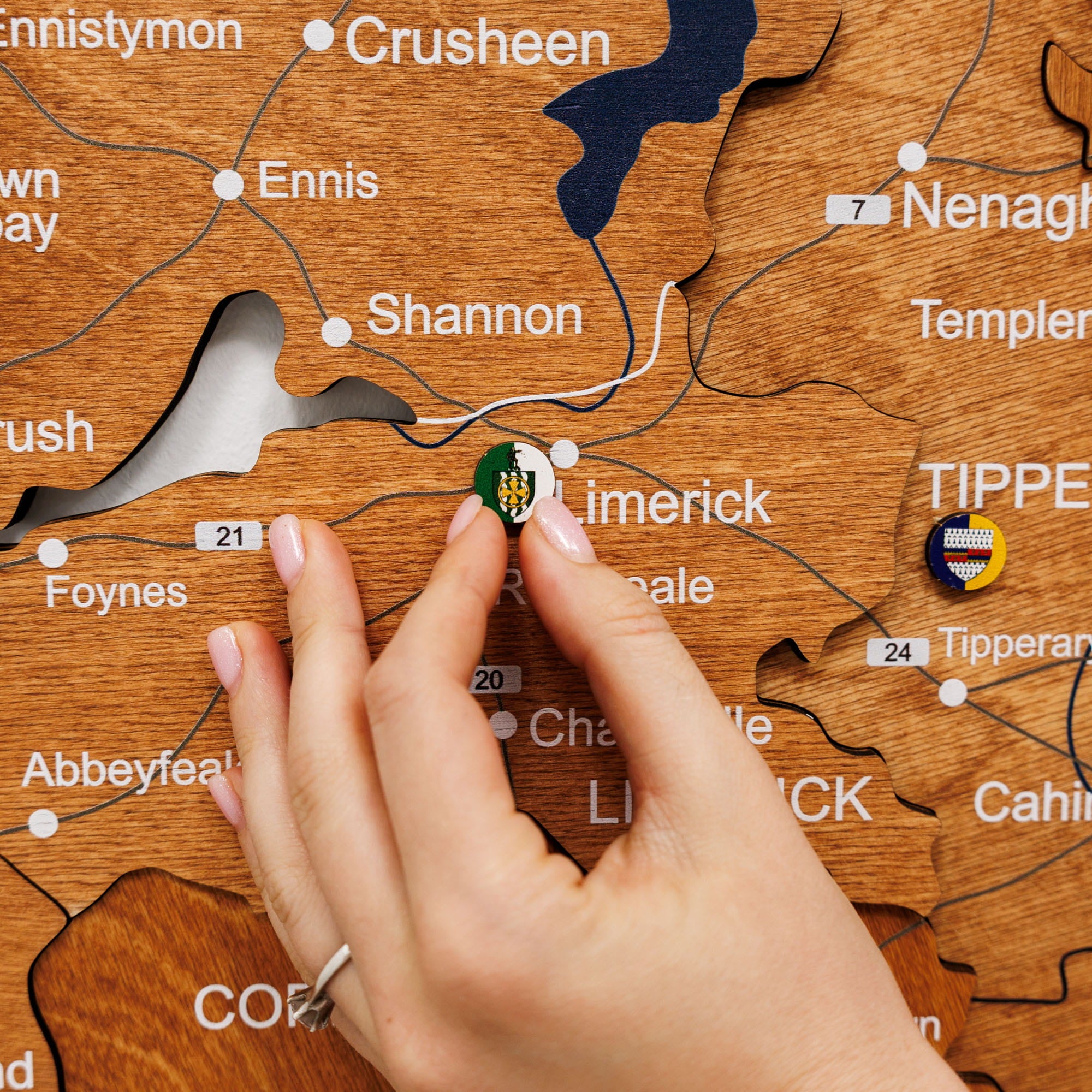 Hand placing a green button on a wooden map of Ireland, with 'Limerick' clearly visible.