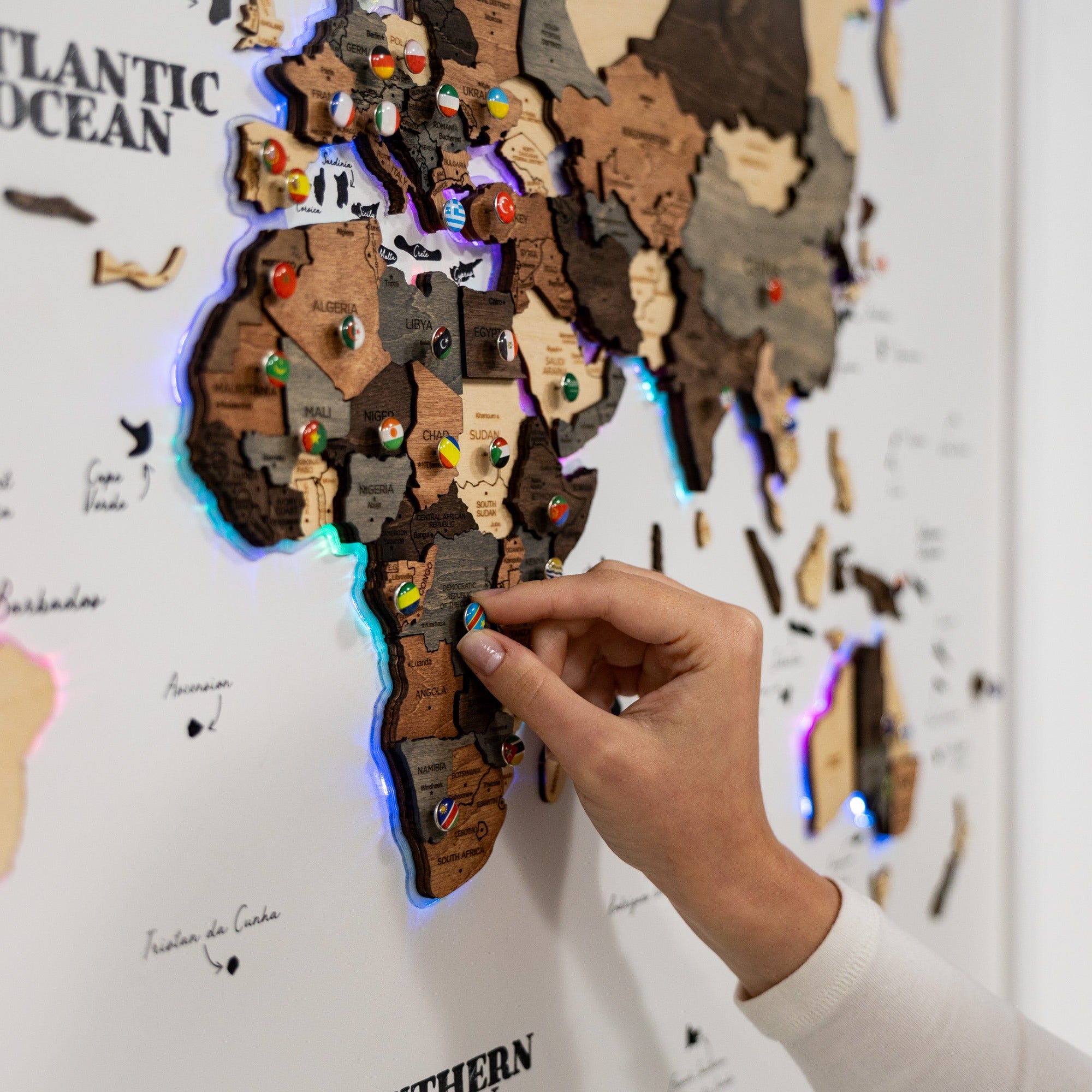 Wooden world map with pinned locations on a wall, illuminated by LED lights.