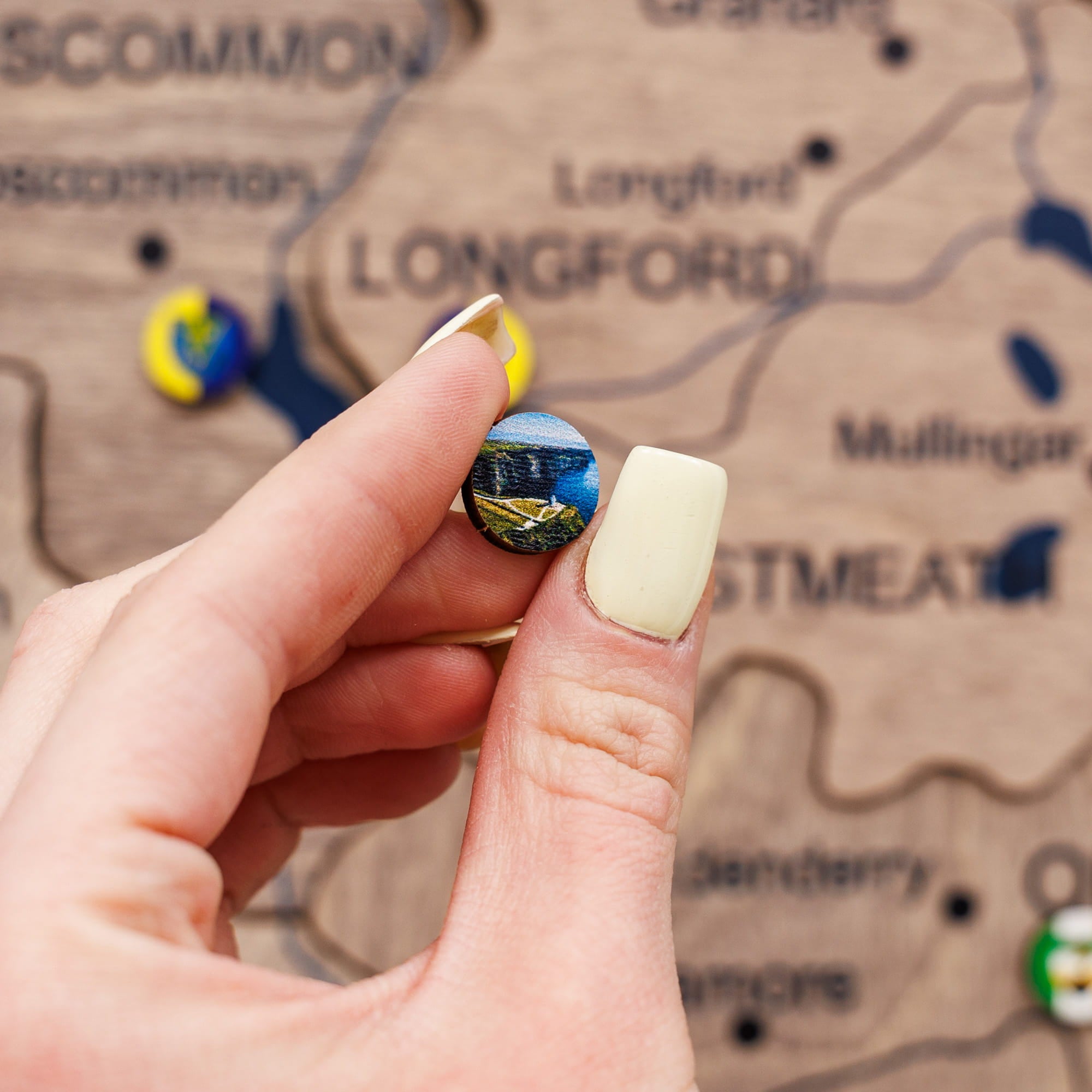 Hand holding a small round object with a scenic design against a map background