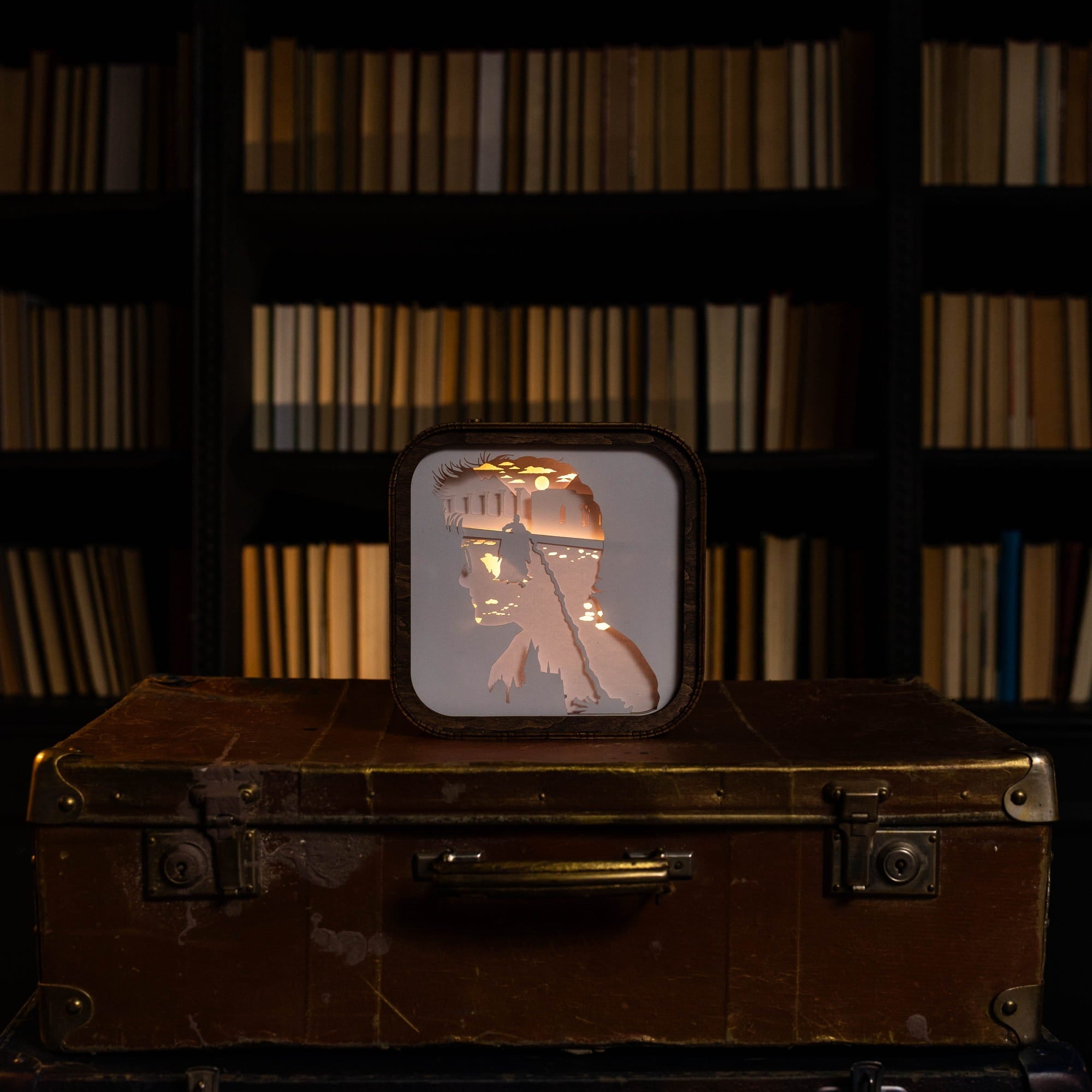 Decorative light box with a geometric design on top of an old suitcase against a bookshelf background.