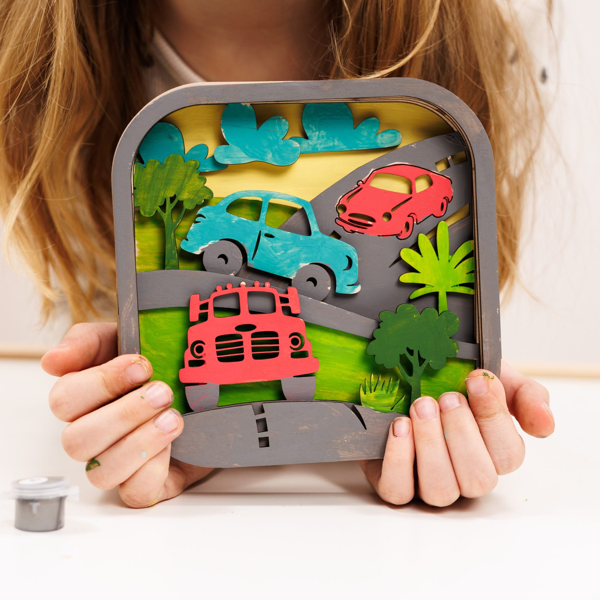 Child holding a toy road with cut-out cars and trees