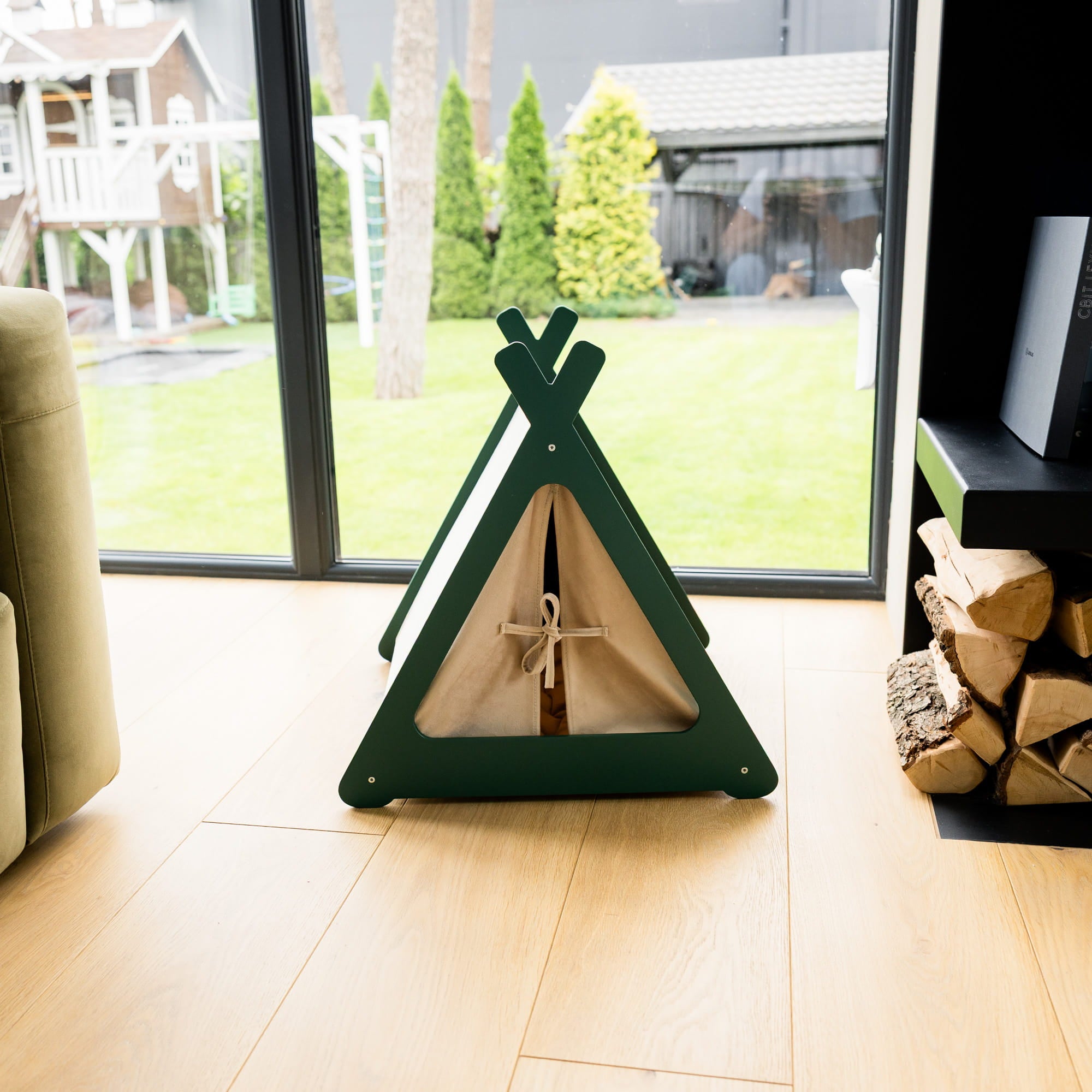 Green pet teepee on a wooden floor with a view of trees outside