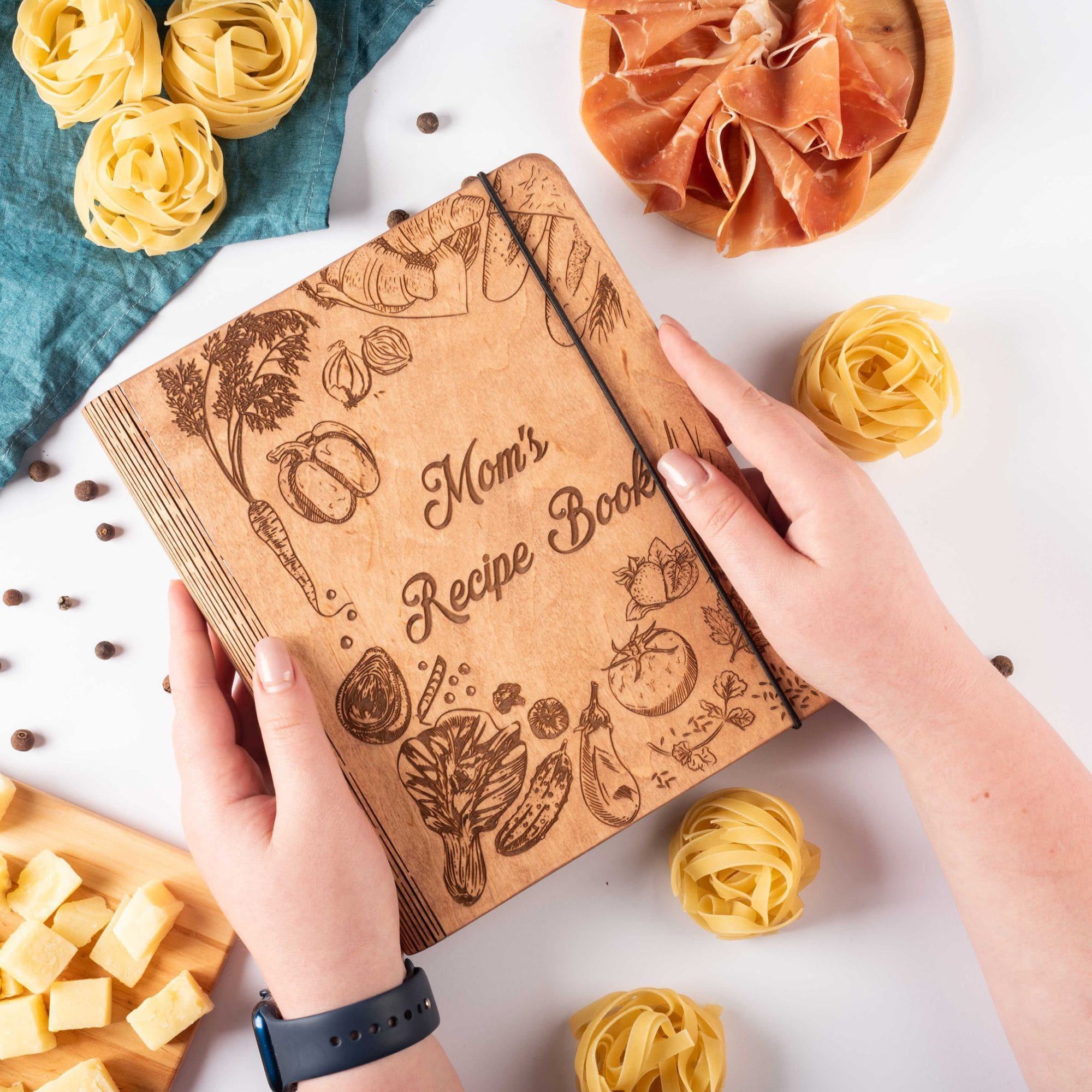 Personalized wooden cookbook held in hands with lemons and herbs