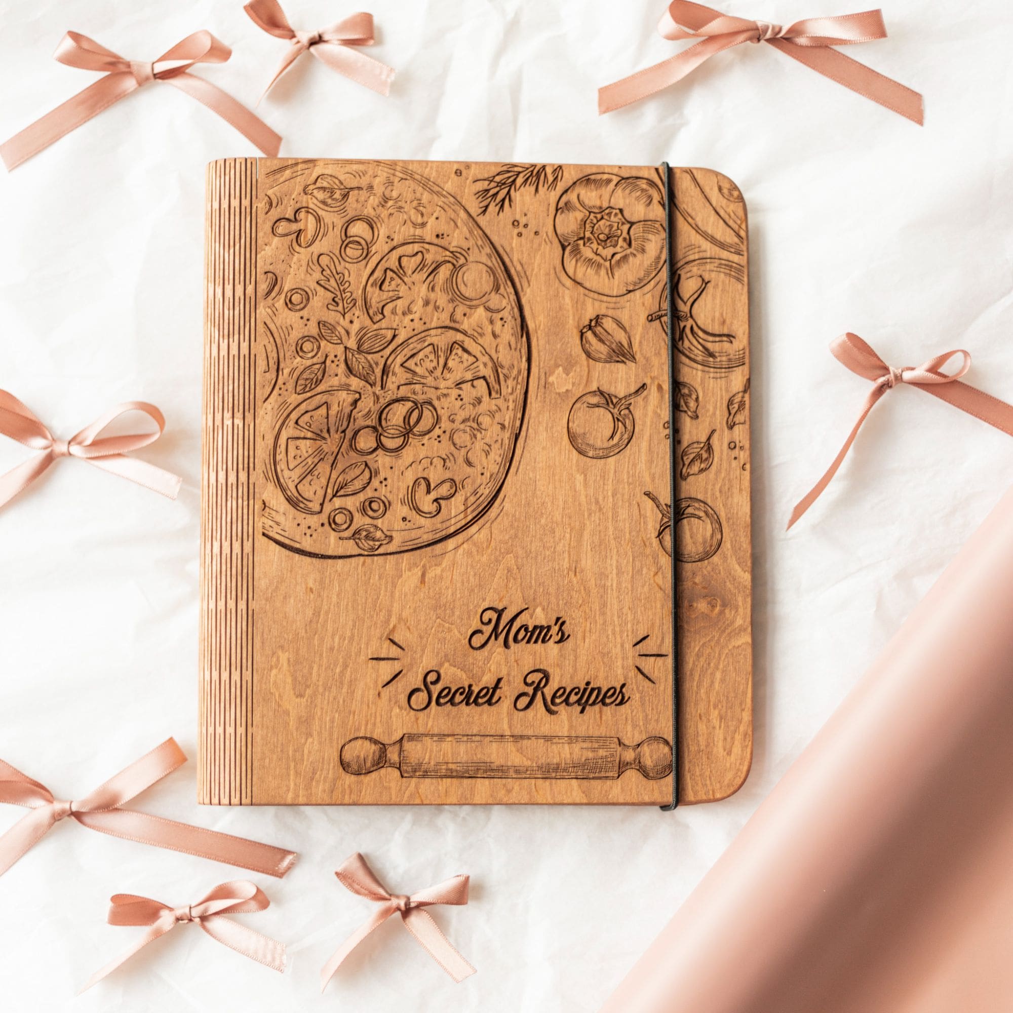 A wooden recipe book with a pizza-themed design, titled 'Mom's Secret Recipes', surrounded by decorative bows on a white background.