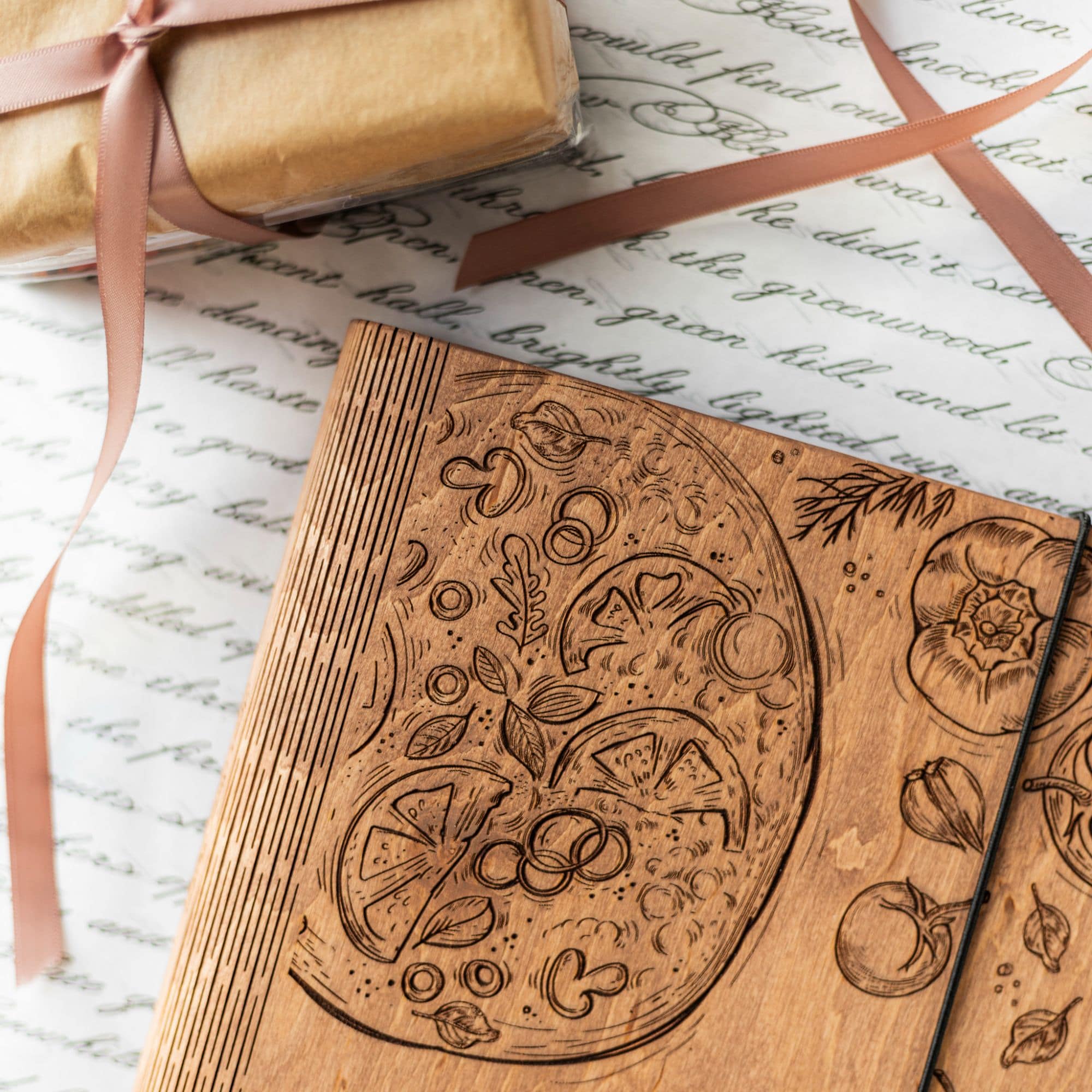 Close-up of engraved wooden recipe book cover with pizza design and vegetables illustration.