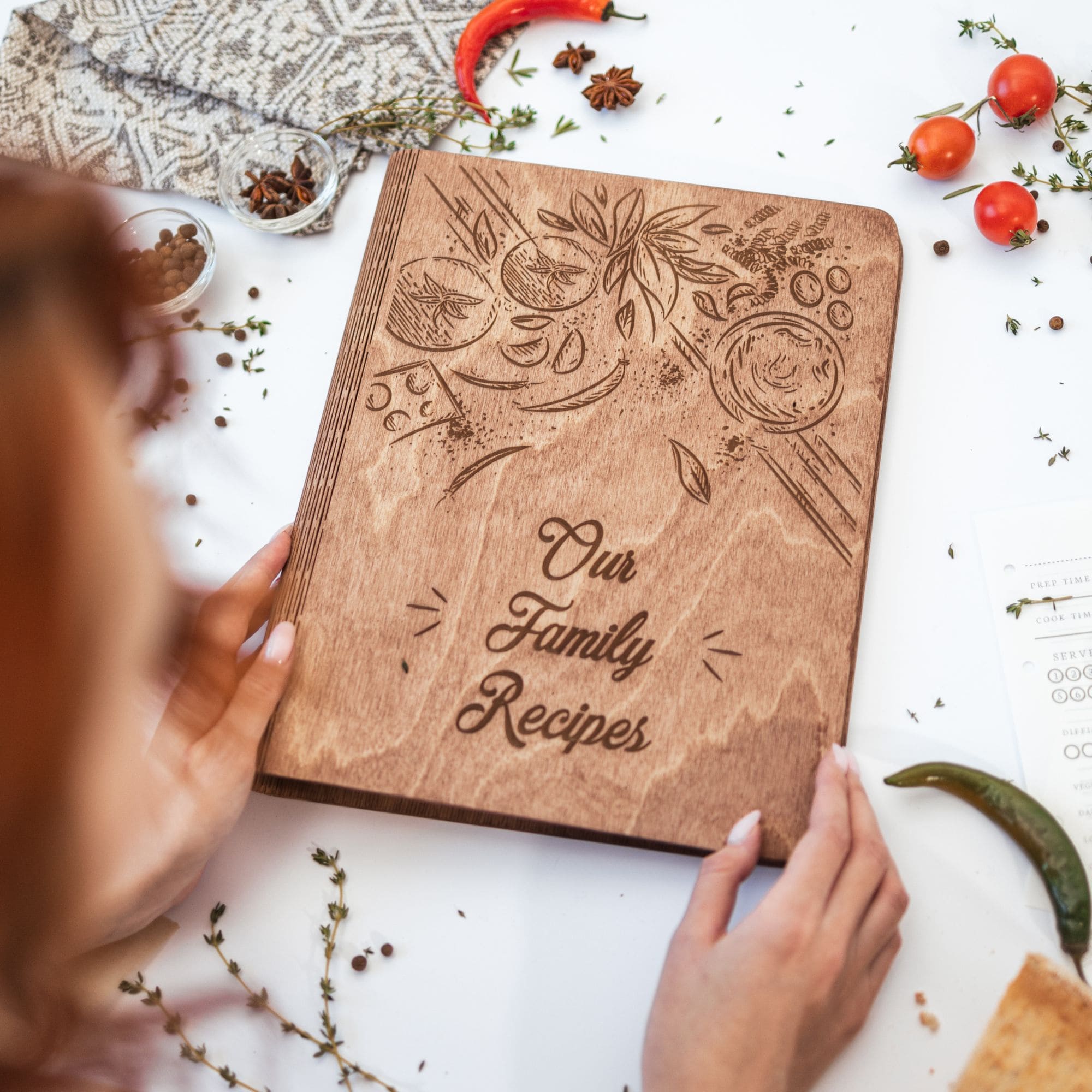 Hand holding engraved wooden recipe book “Our Family Recipes” – rustic personalized family cookbook