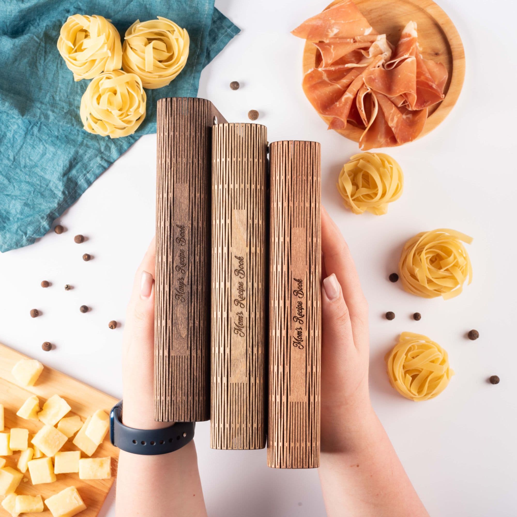 Set of engraved wooden recipe books standing on table with pasta and cheese – custom cookbook collection