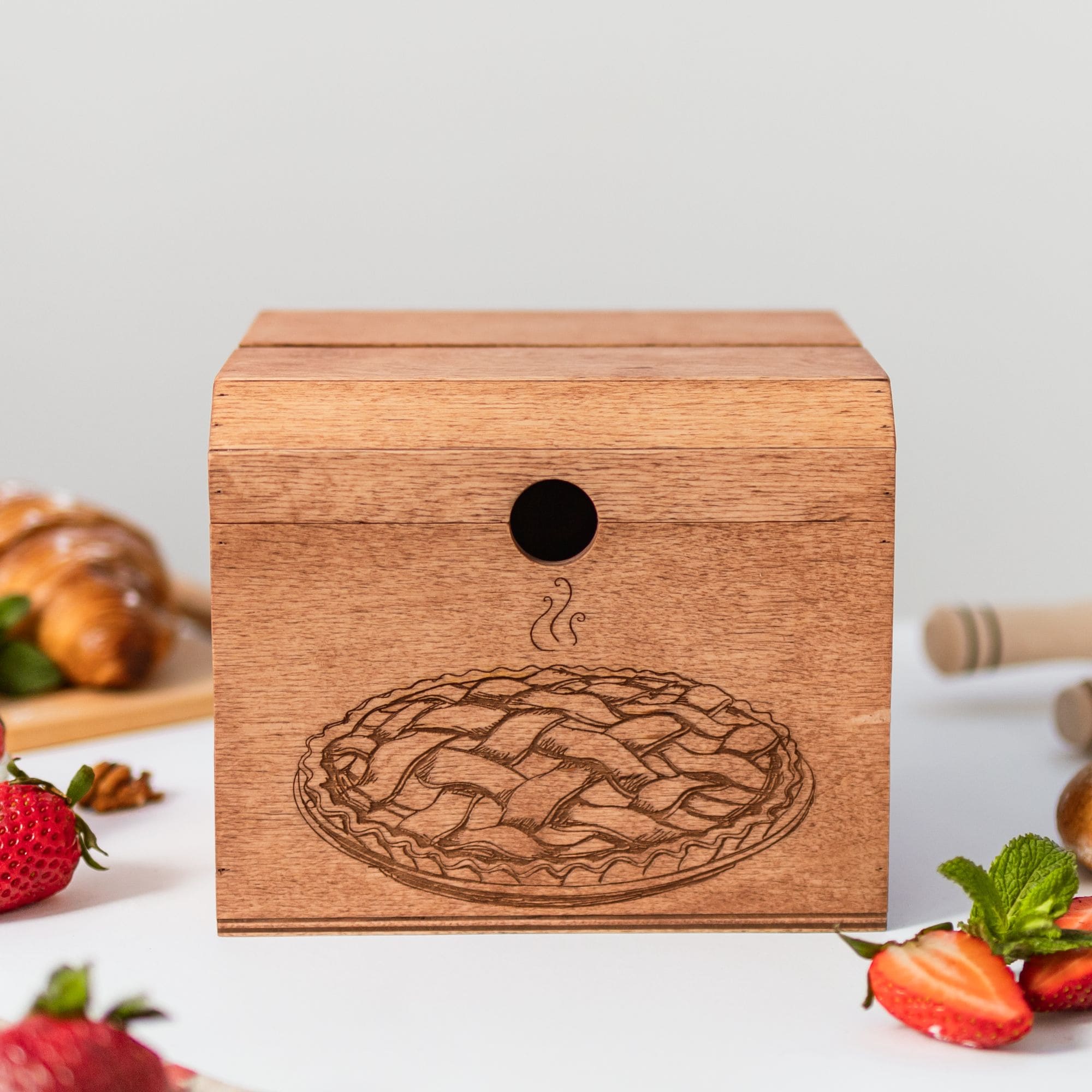 Closed wooden recipe box with pie engraving on table with fresh strawberries.