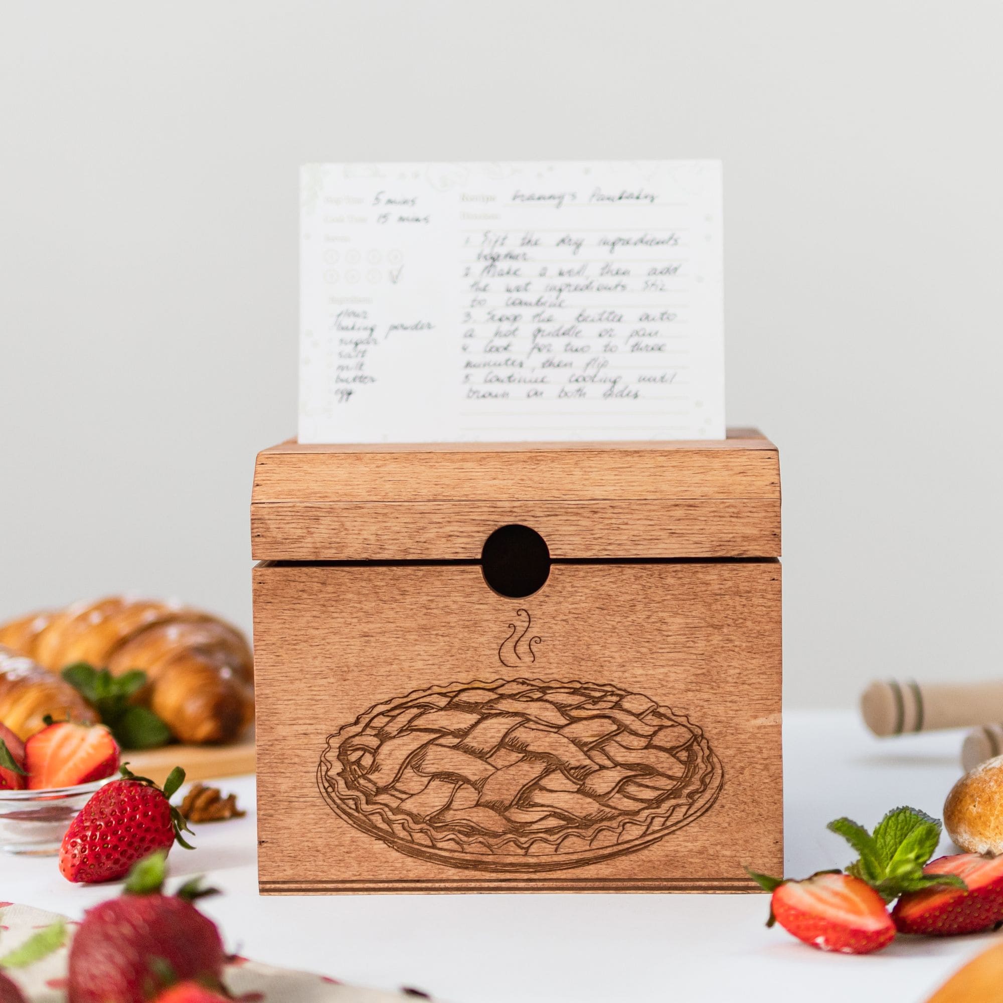 Recipe box with engraved pie design and recipe card placed on top.