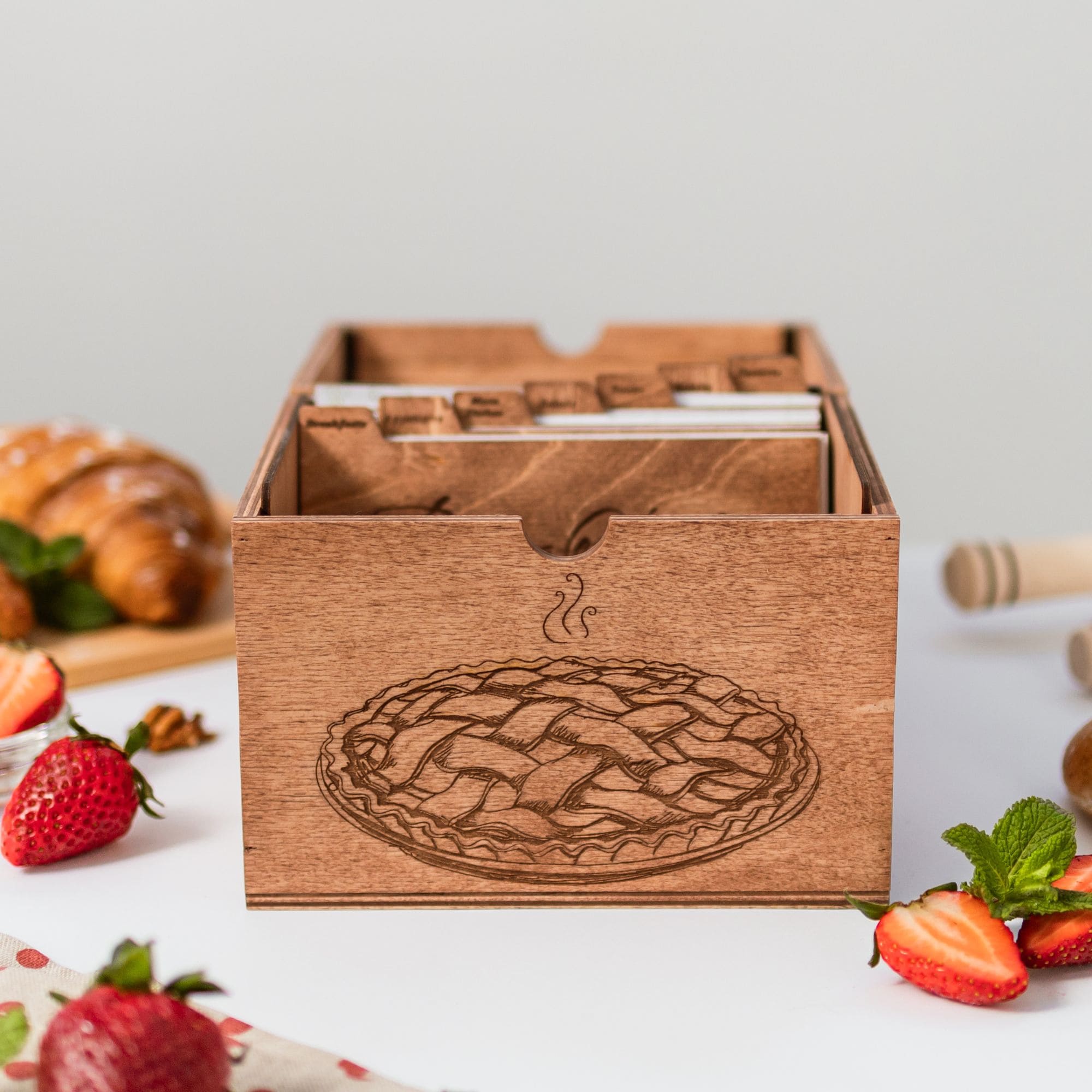 Open wooden recipe box holding recipe cards, surrounded by pastries and strawberries.
