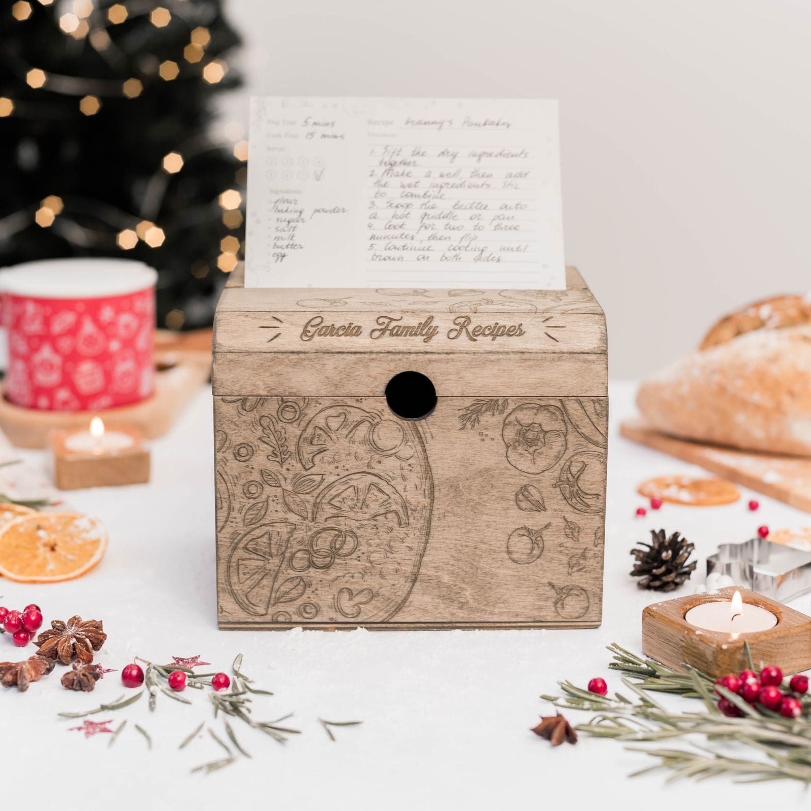 A wooden recipe box with a pizza-inspired design, displayed on a table with festive decorations, including a cup, oranges, and candles. The box is open, revealing a written recipe inside.