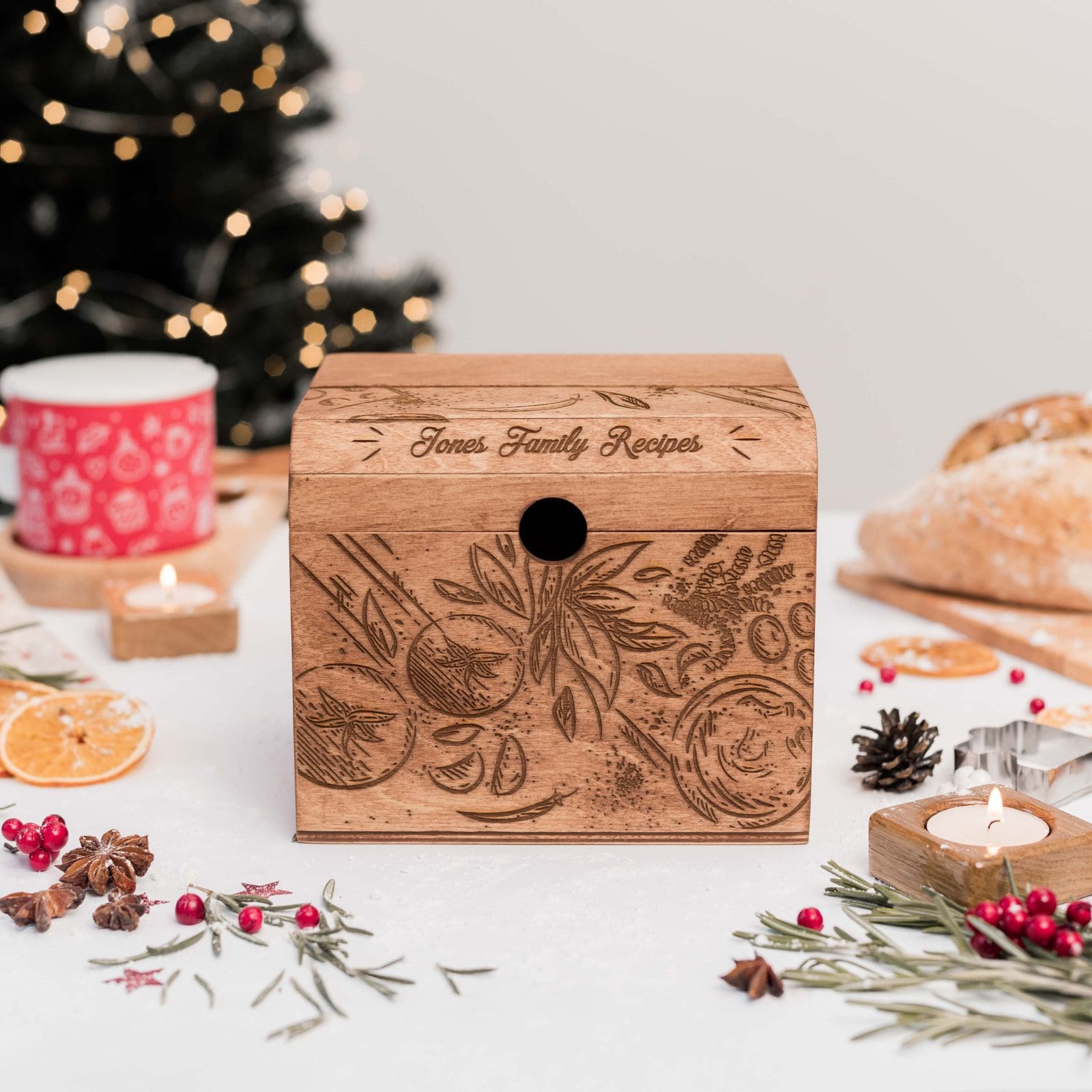A wooden recipe box with a tomatoes design, displayed on a table with festive decorations, a cup of tea, and baking ingredients.