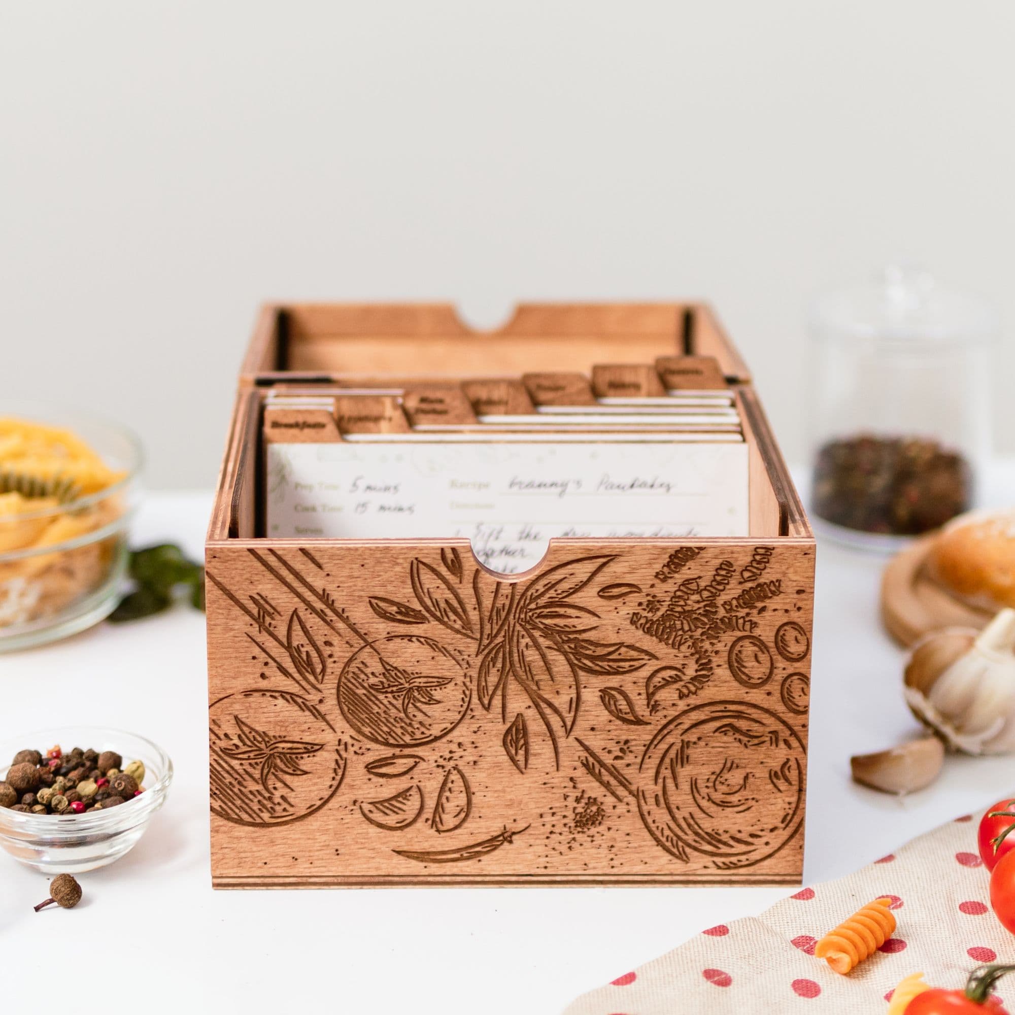 Wooden recipe box with engraved design and recipe cards inside on kitchen table