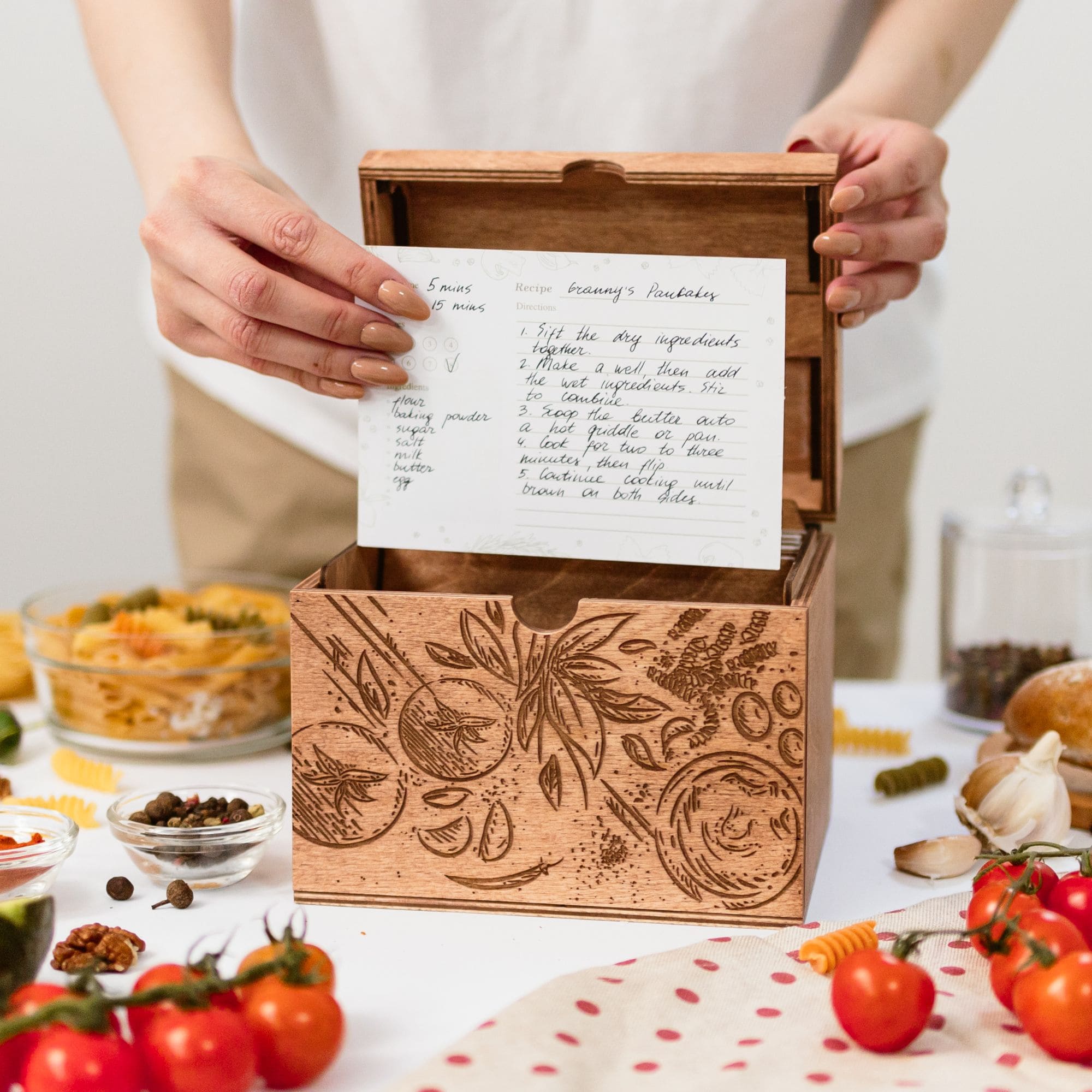 Person holding handwritten recipe card above engraved wooden recipe box