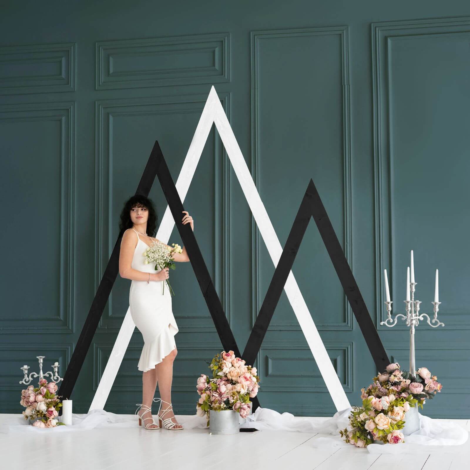 Bride holding bouquet beside stylish black white triangle arches.