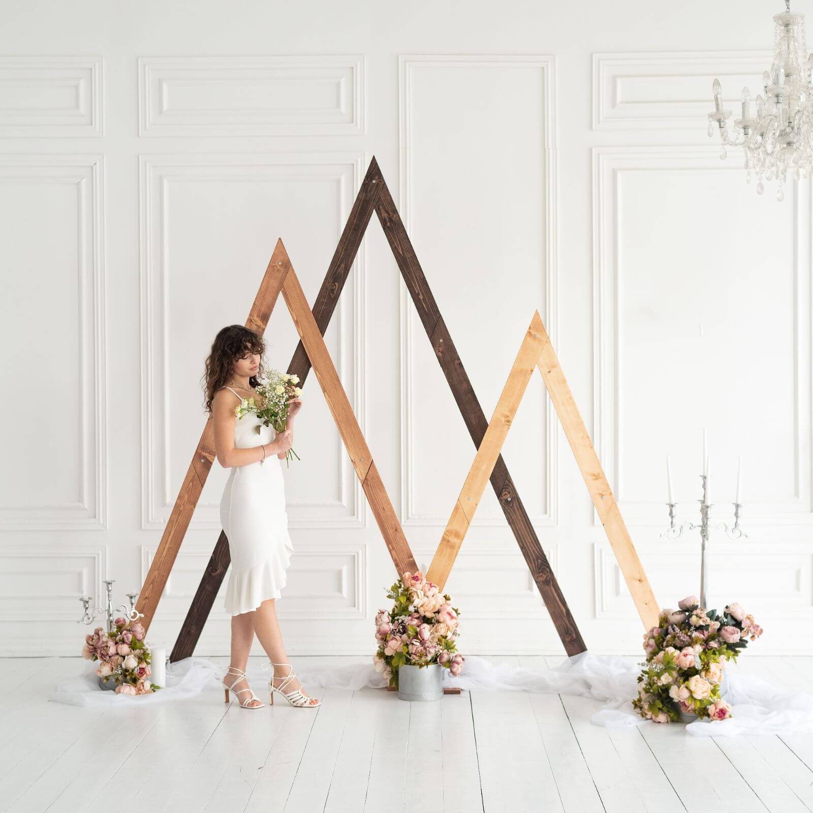 Bride in elegant dress posing near wooden triangle arches.