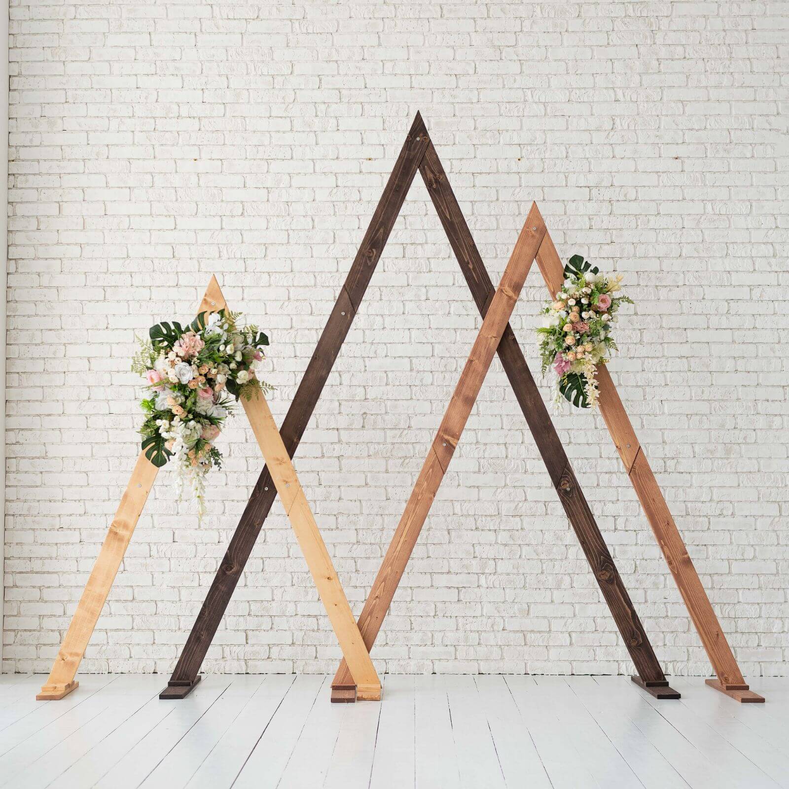 A modern triangle-shaped wedding arch made of wood, available in different colors, with floral decorations on top.