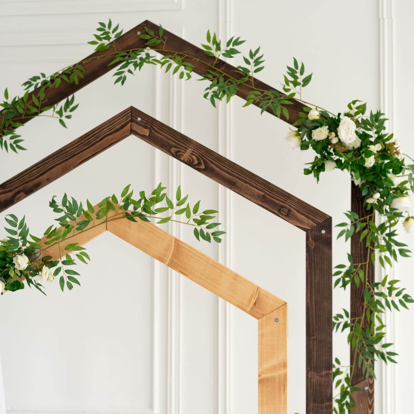 Wooden pentagon wedding arches decorated with greenery and flowers.